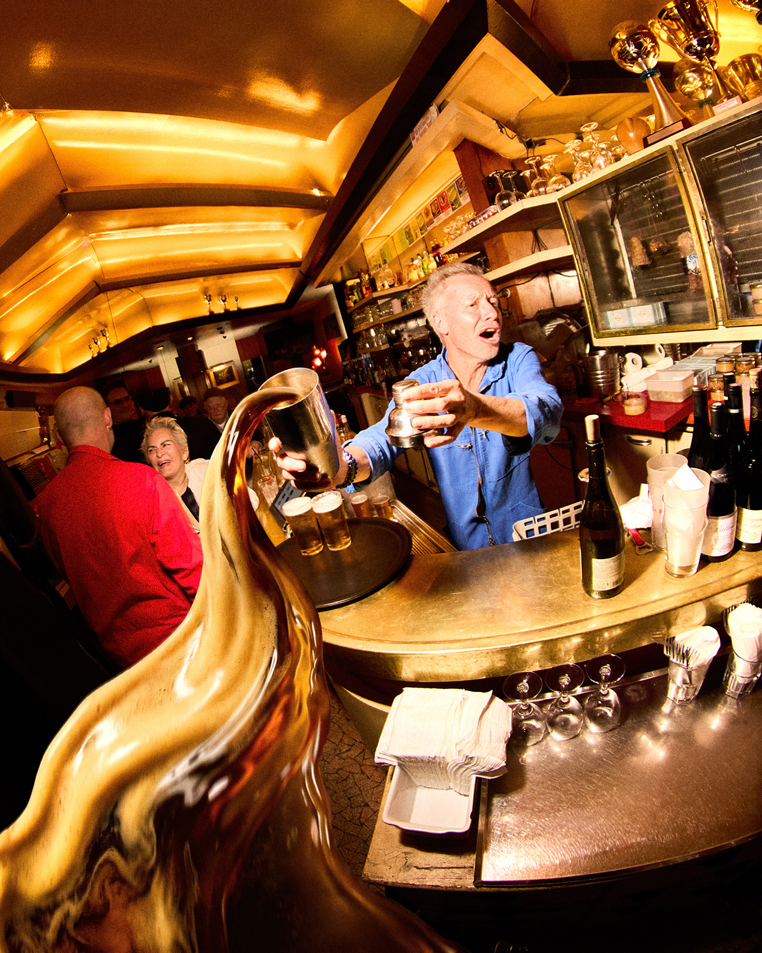 Barman servant derrière un comptoir en laiton, éclaboussure de bière, intérieur de brasserie parisienne