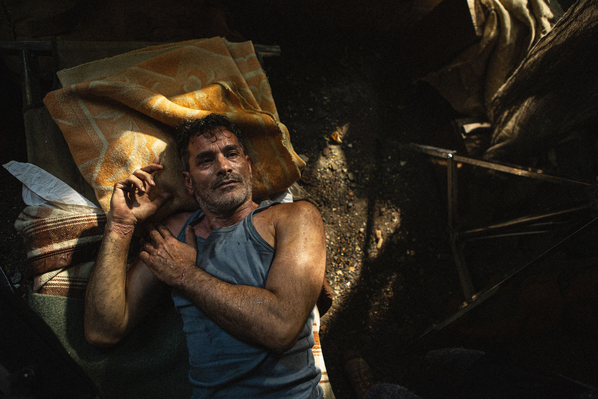 Actor Koen De Bouw lying on a field bed with a yellow blanket.