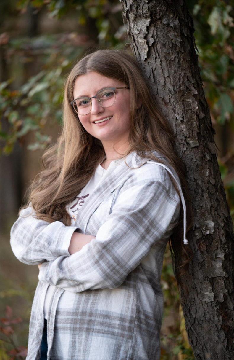 A young woman is leaning against a tree while smiling