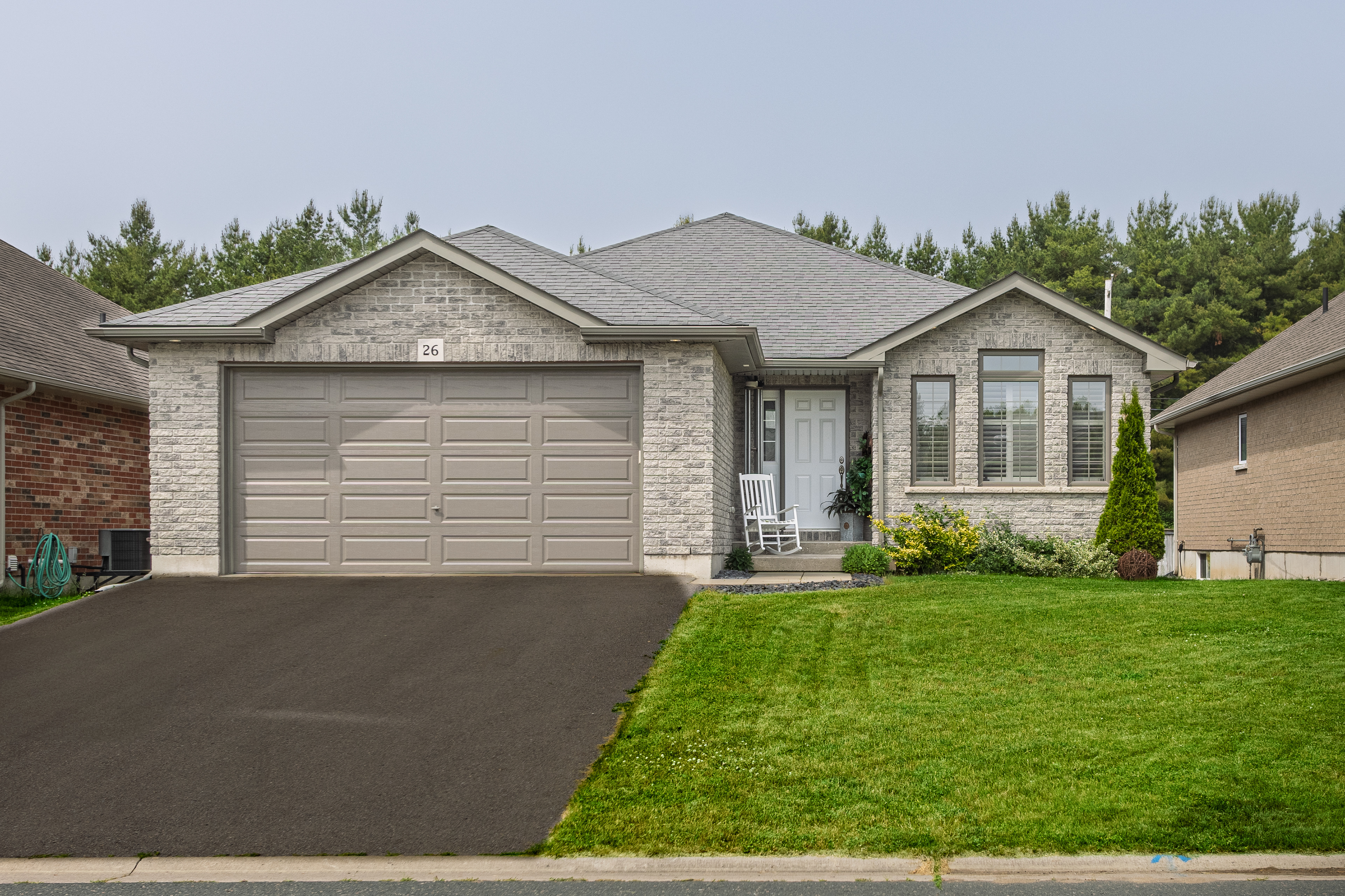 Daytime exterior photo of single-family home in Brighton Ontario with gray brick and double garage