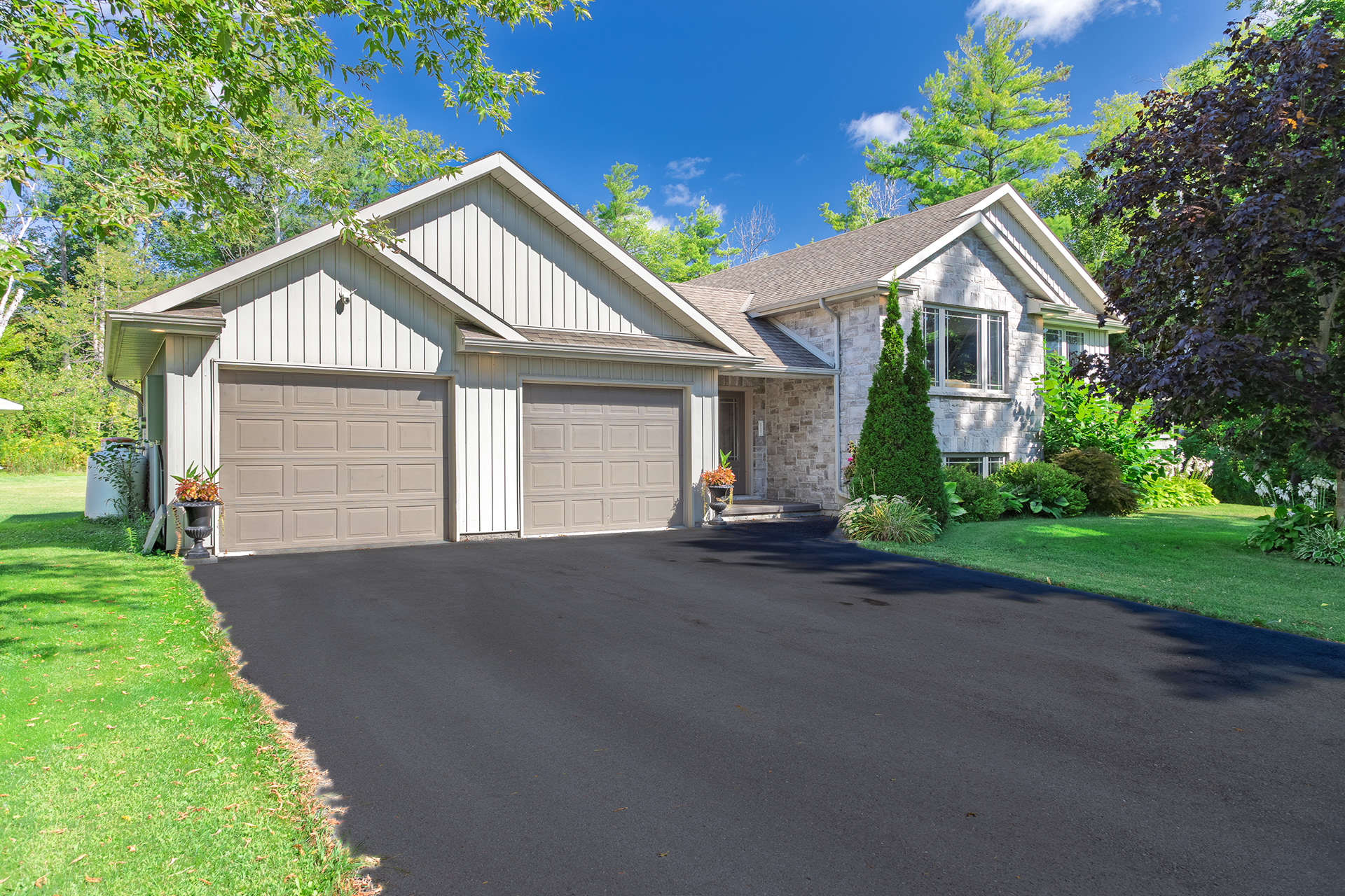 Daytime photo of light stone home in Brighton with triple garage and lush green landscaping