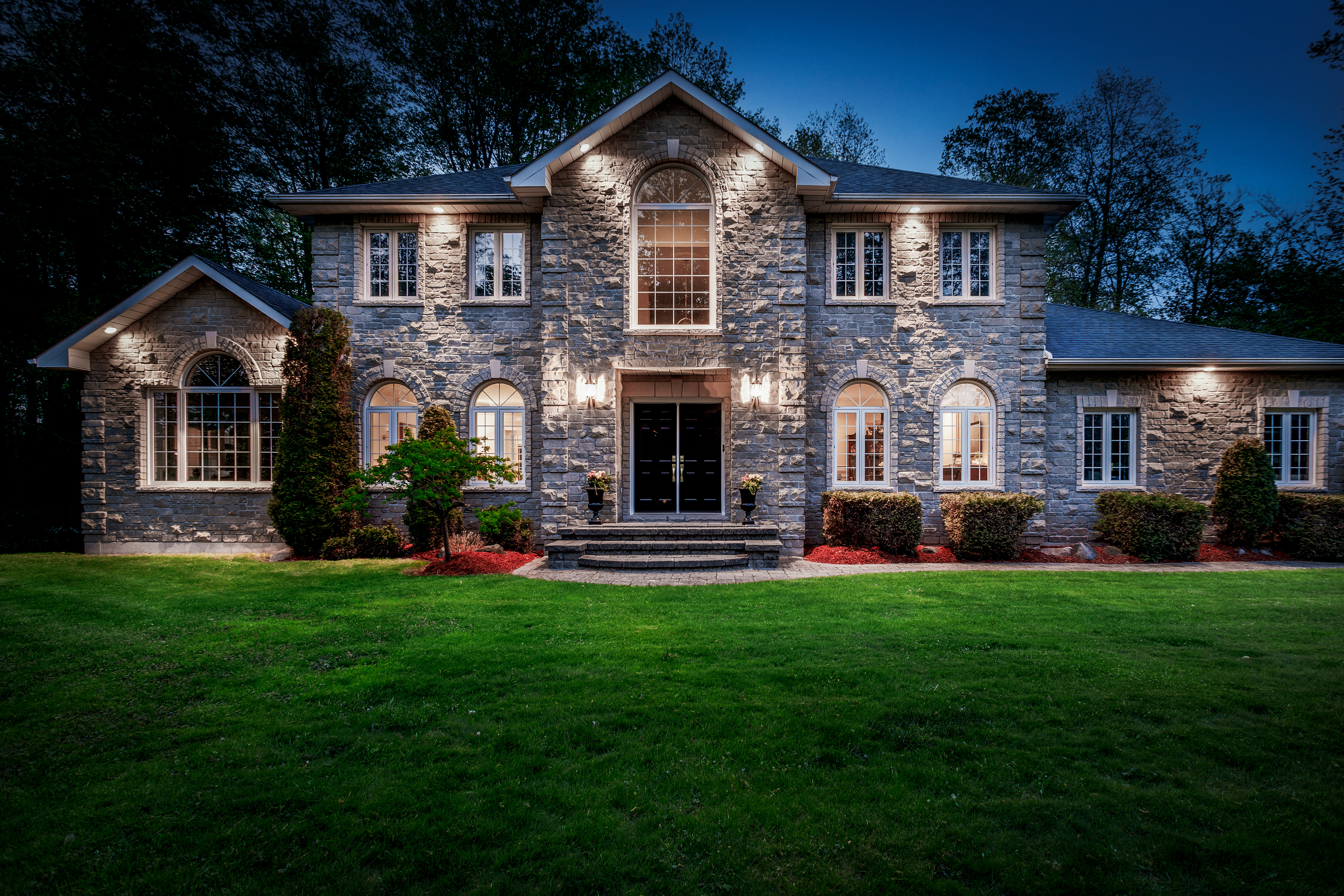 Twilight lighting enhances the scale, symmetry, and architectural detail of this grand stone residence.
