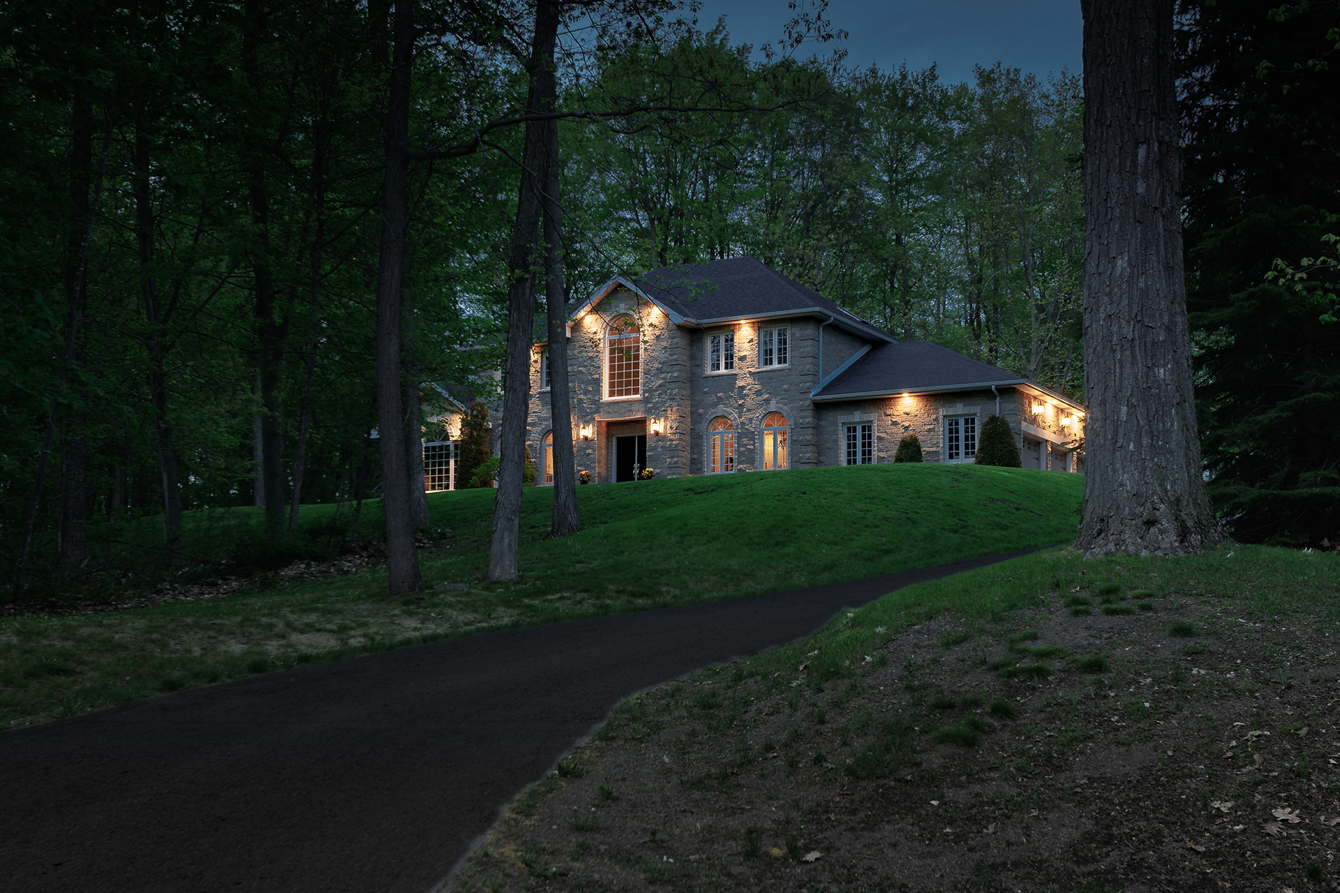 Warm architectural lighting emerges through the trees as evening settles over this secluded woodland property.