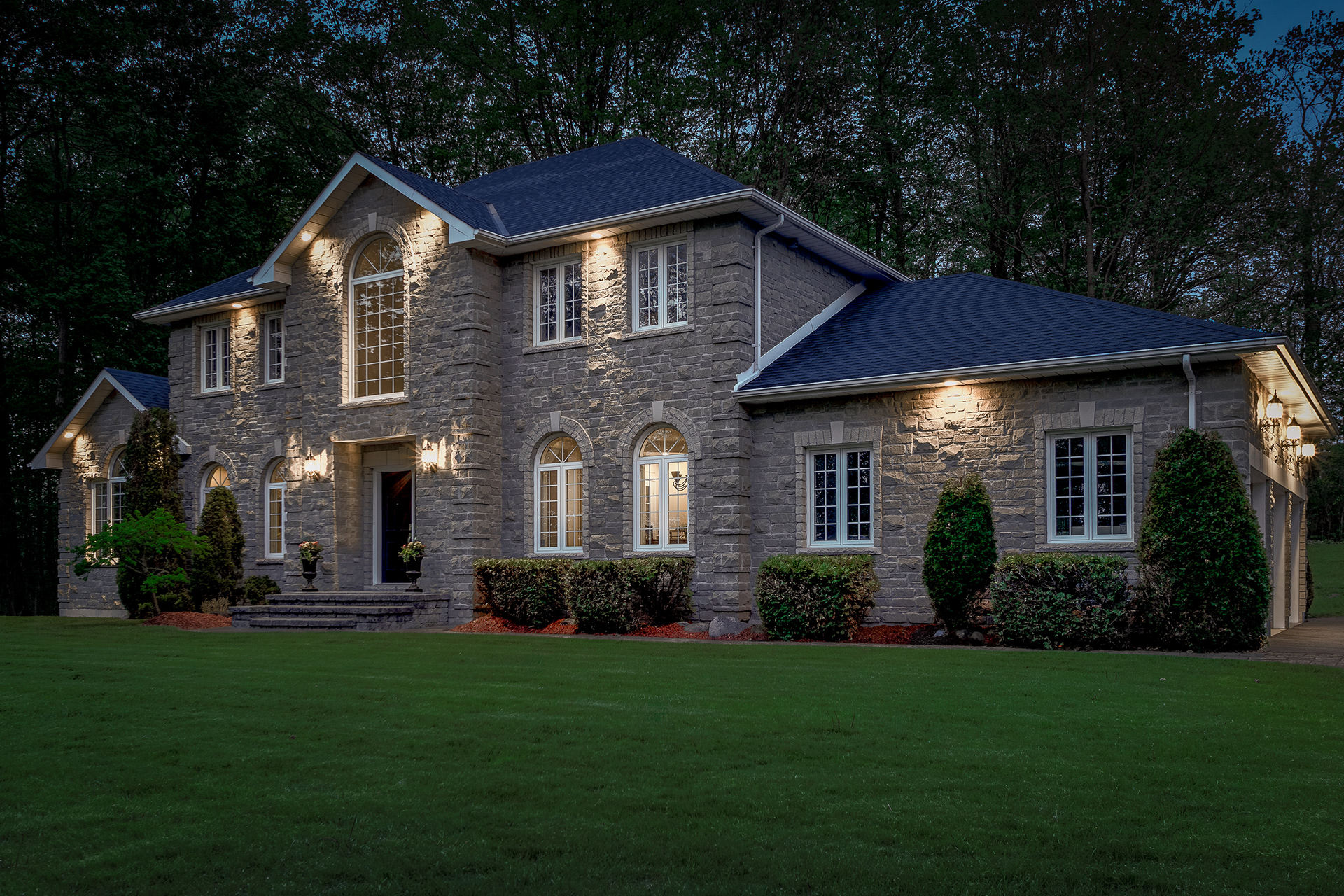 Evening architectural lighting highlights the texture, form, and character of this stone residence at blue hour.
