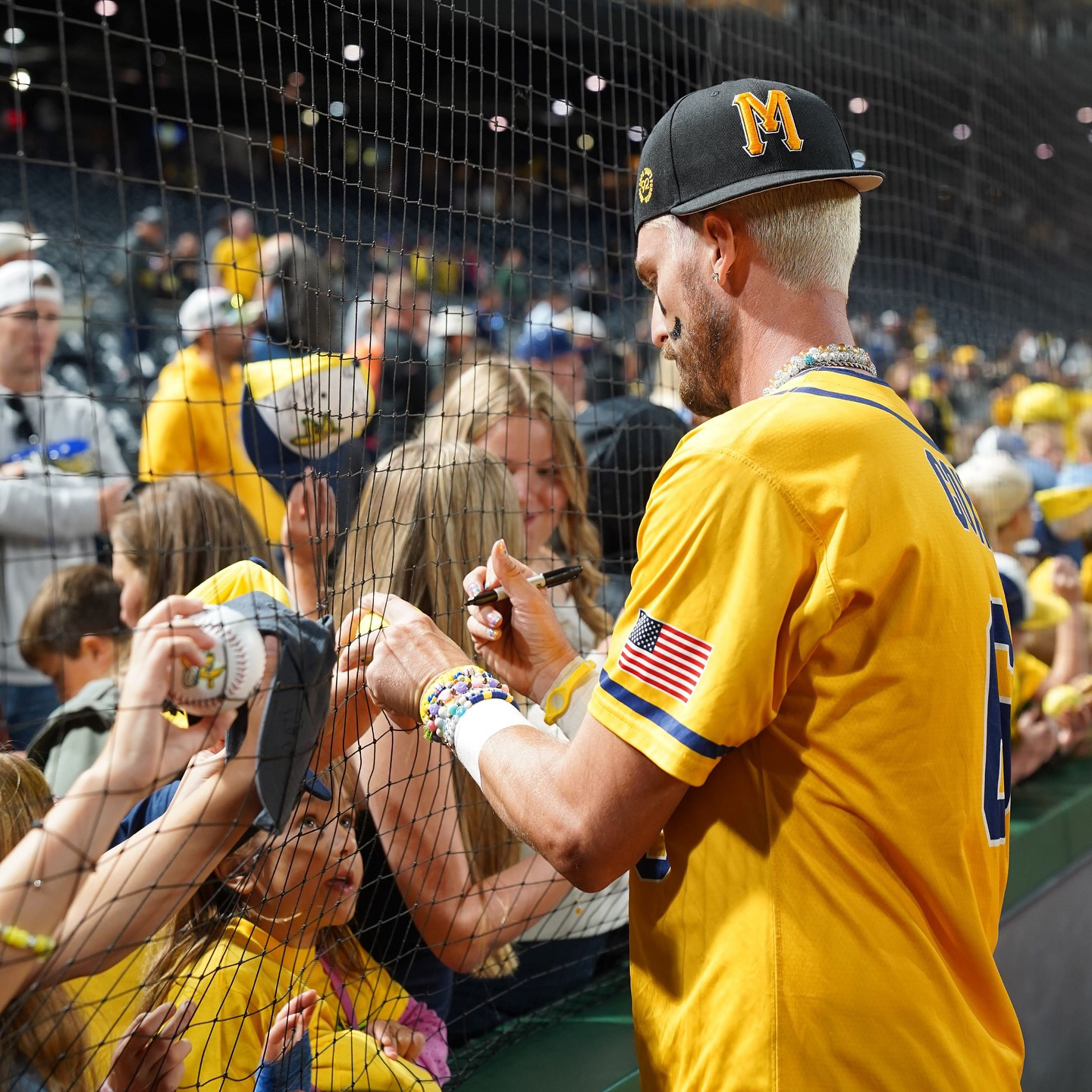 Ryan Cox of the Savannah Bananas signing autographs for eager fans, wearing a yellow uniform jersey with a custom Rooted in Pittsburgh x Mac Miller M hat at PNC Park, 2025