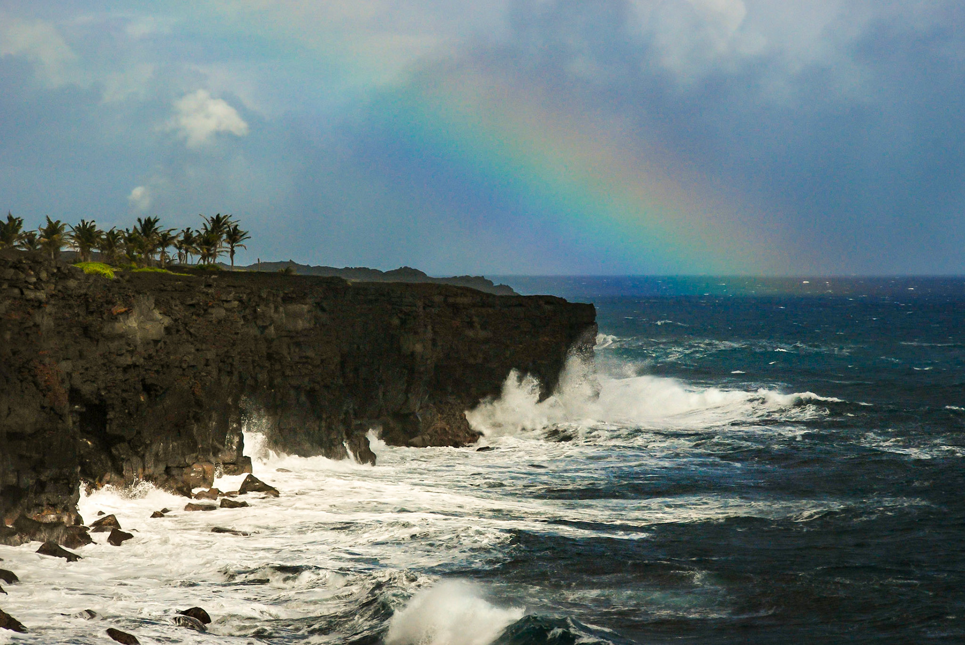 A rainbow arcs over Hawaii's Big Island as Pacific Ocean waves pelt the rocky shore build by lava flows.