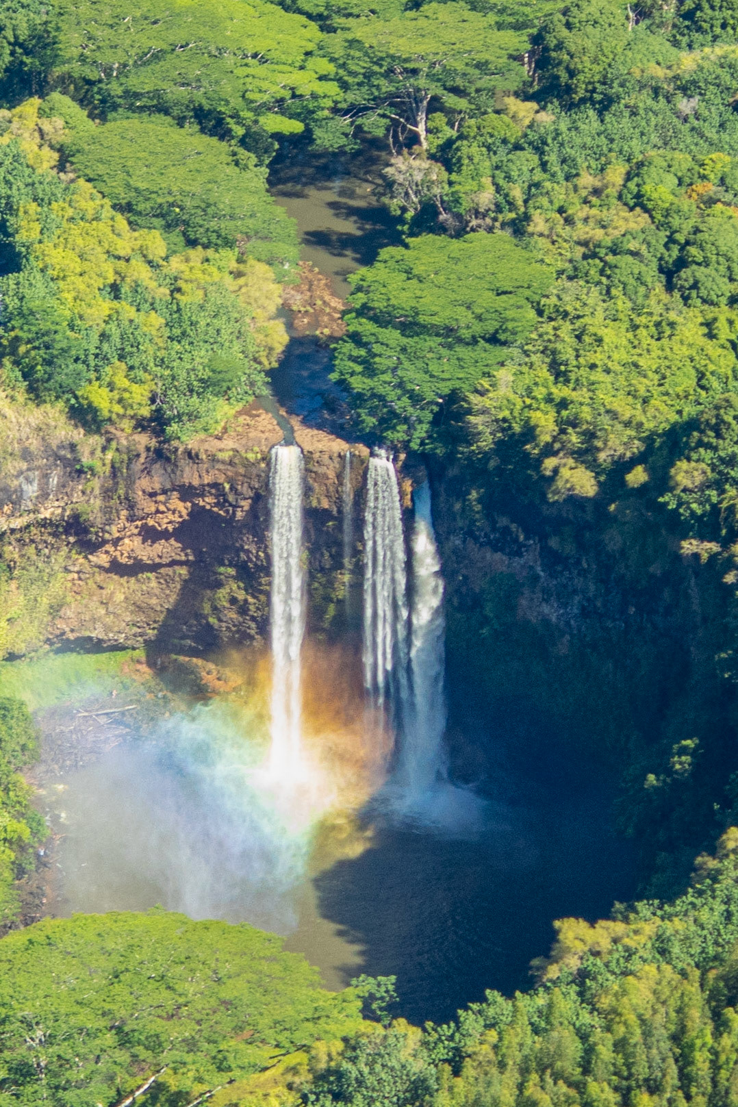 Wailua Falls plunge into a pool as the sun creates a rainbow in the mist.