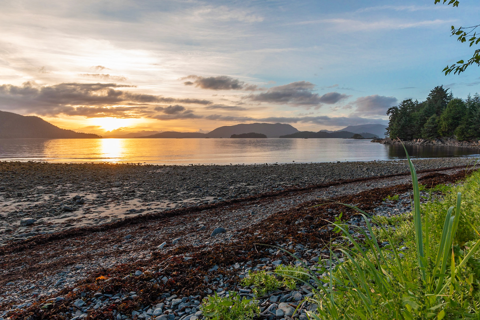 The colors of a Sitka beach warm up as the sun sets behind distant islands of Alaska.