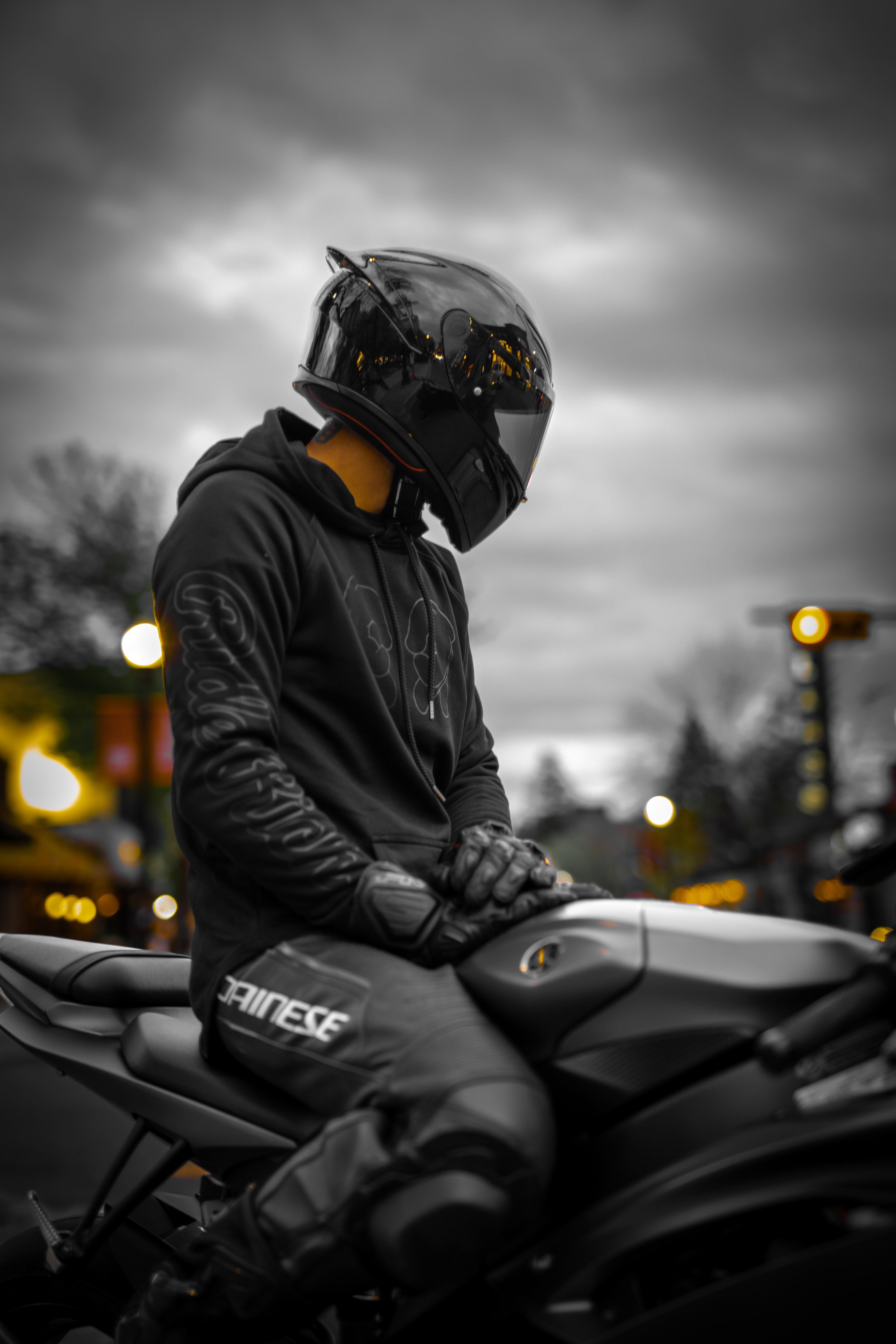 Motorcycle rider in black helmet and Dainese gear sitting on a matte sportbike in downtown Calgary during a moody evening ride.