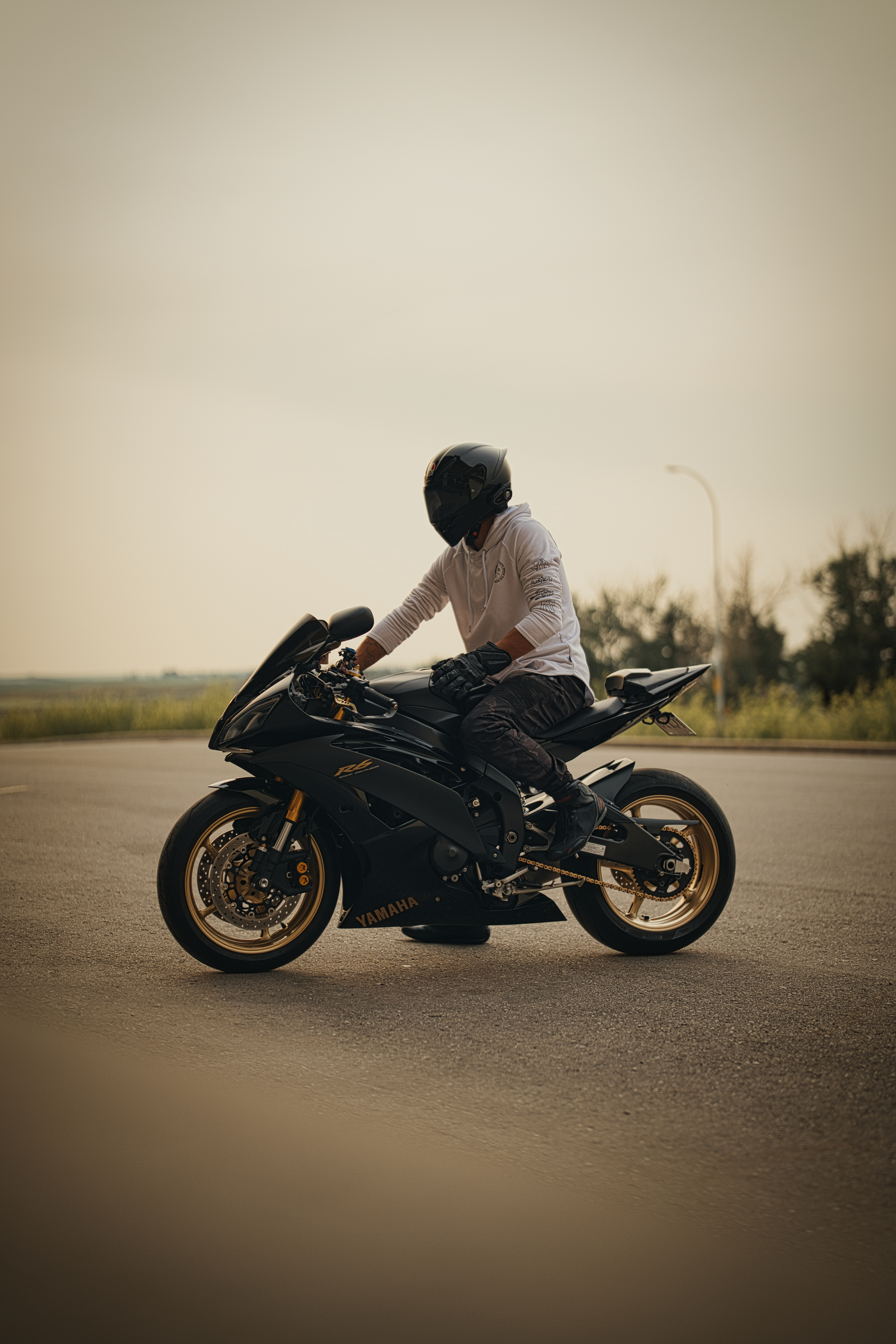 Golden hour motorcycle photography in Calgary by Black Rev Studio—rider in white hoodie with full-face helmet straddling a matte black Yamaha R6 sportbike.