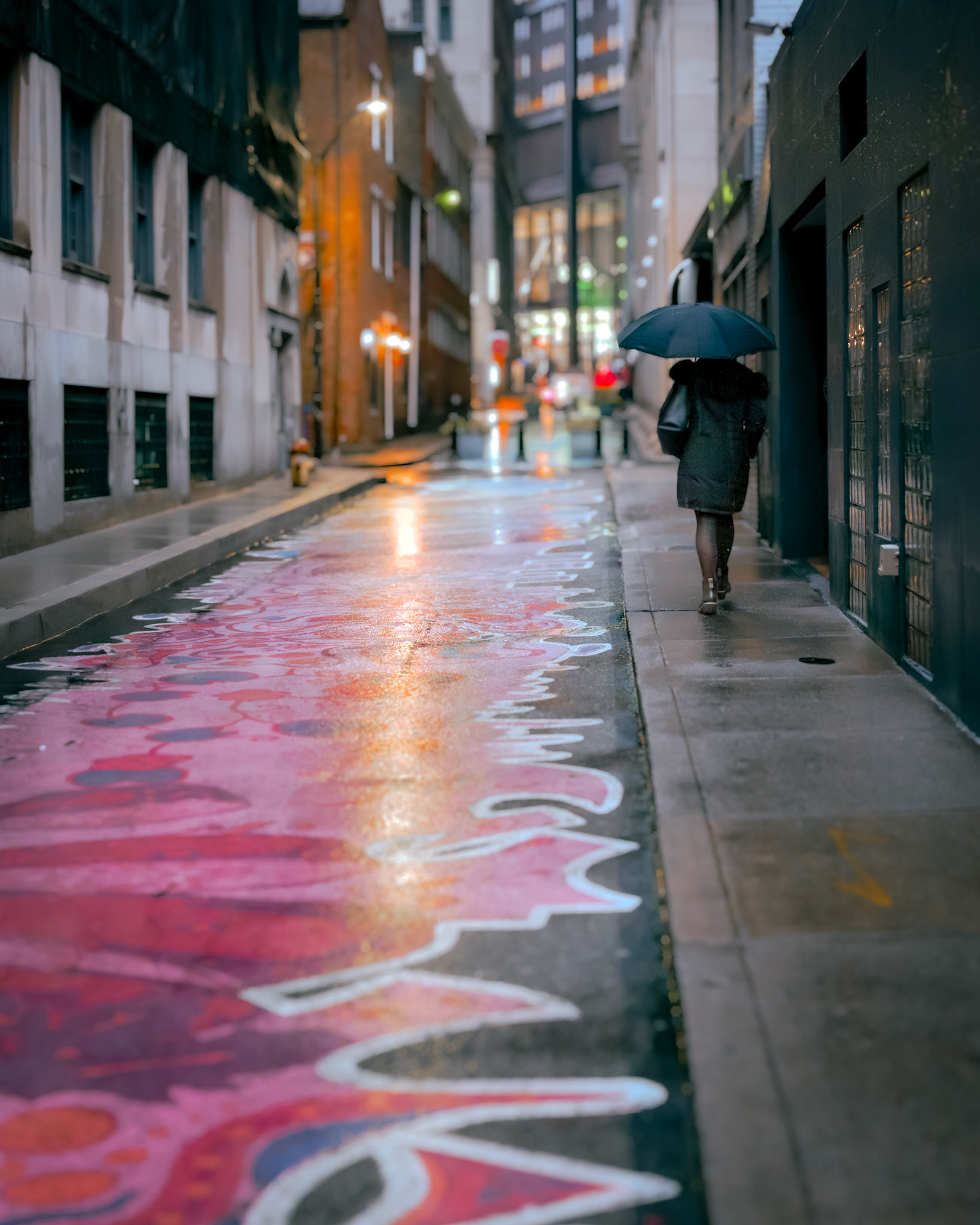 Rain deepens the colors, turning the painted pavement into a liquid canvas. A solitary figure walks the winding path, umbrella in hand, moving between neon reflections and soft streetlights. In the city’s quiet alleys, art and life blend, and every step becomes part of the story.