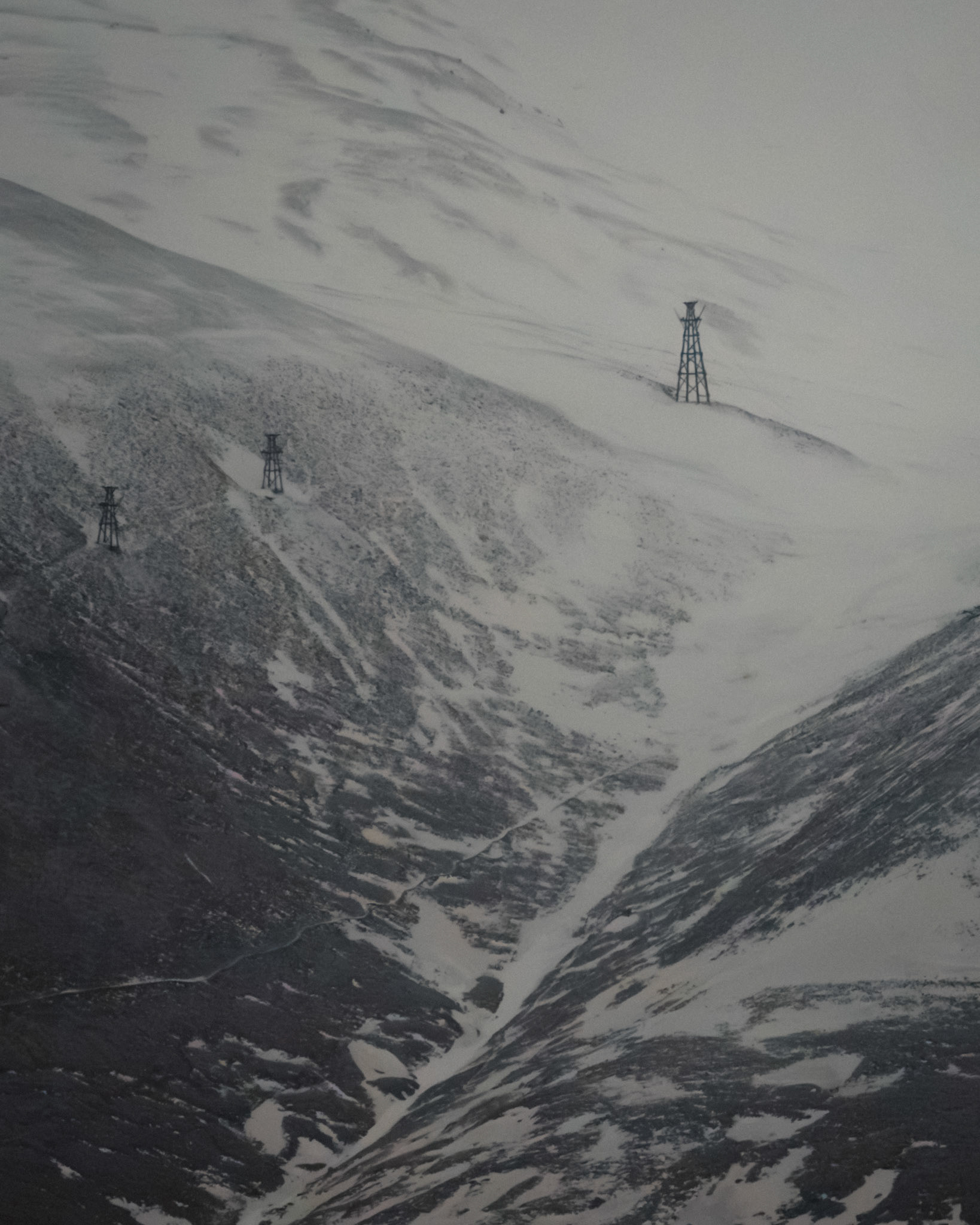 The skeletal remains of a once-thriving lifeline stand against the Arctic winds. These abandoned coal towers, relics of Svalbard’s mining past, now fade into the snow—silent witnesses to a world that has moved on. The land reclaims what is left behind, but the structures endure, holding their place between history and oblivion.