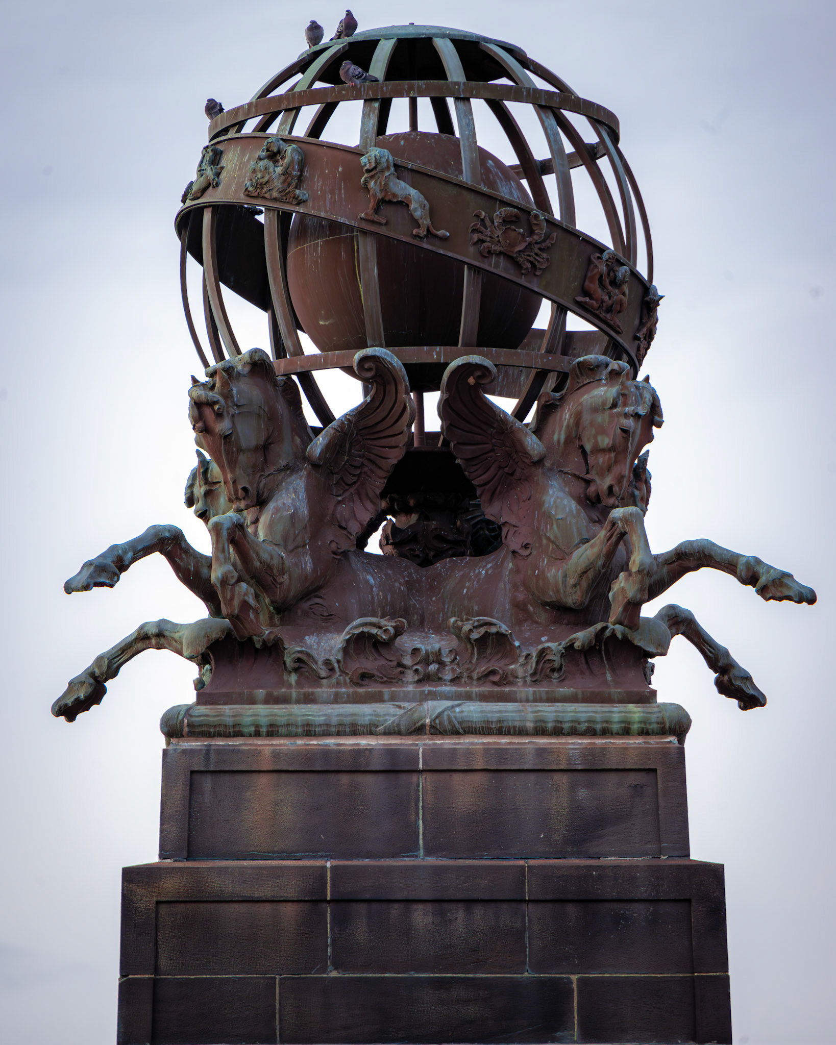 Perched atop their pedestal, these winged creatures seem to hold up the world itself. Weathered by time, their bronze bodies bear the weight of history, a silent testament to Pittsburgh’s architectural grandeur. The celestial sphere above, adorned with symbols of the zodiac, evokes a sense of cosmic order, watched over by a council of ever-present pigeons.