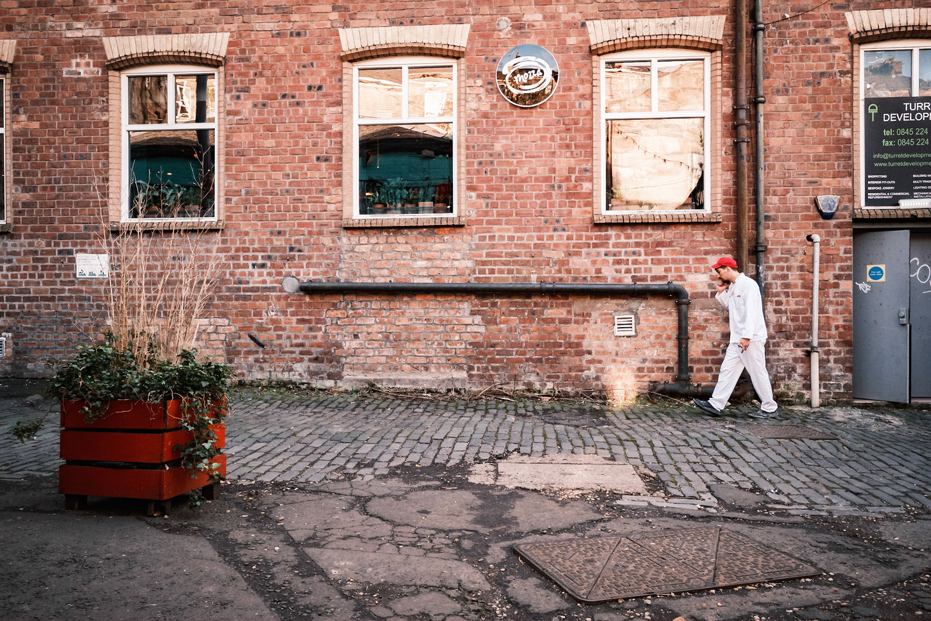 Intense cook taking two minutes away from the Kitchen. I liked the matching red of the hat, building and planter.