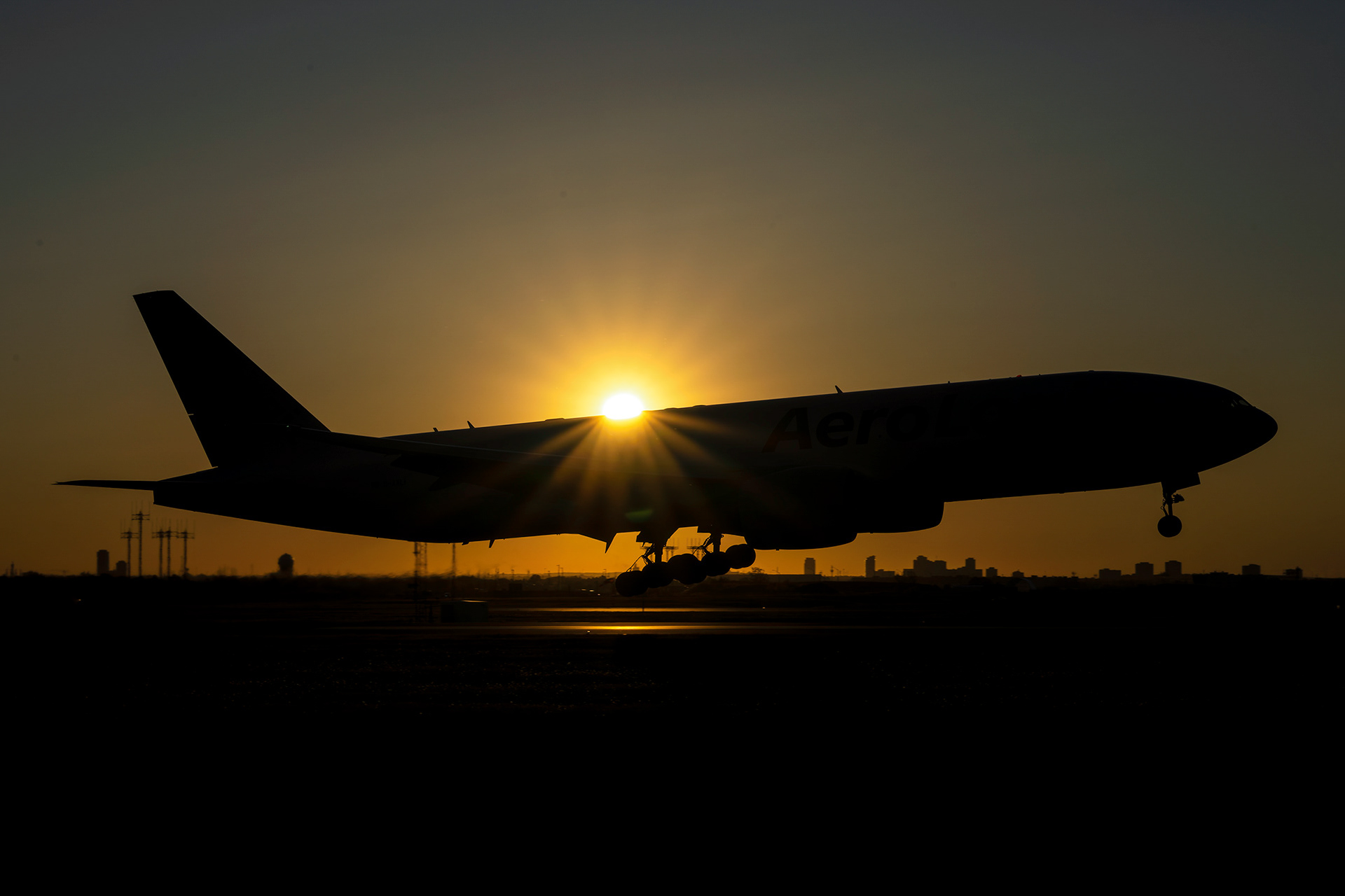 An AeroLogic Boeing 777F wide-body cargo freighter is captured in a striking silhouette against a brilliant golden sunset. Commercial aviation photography by Kevin Prentice.