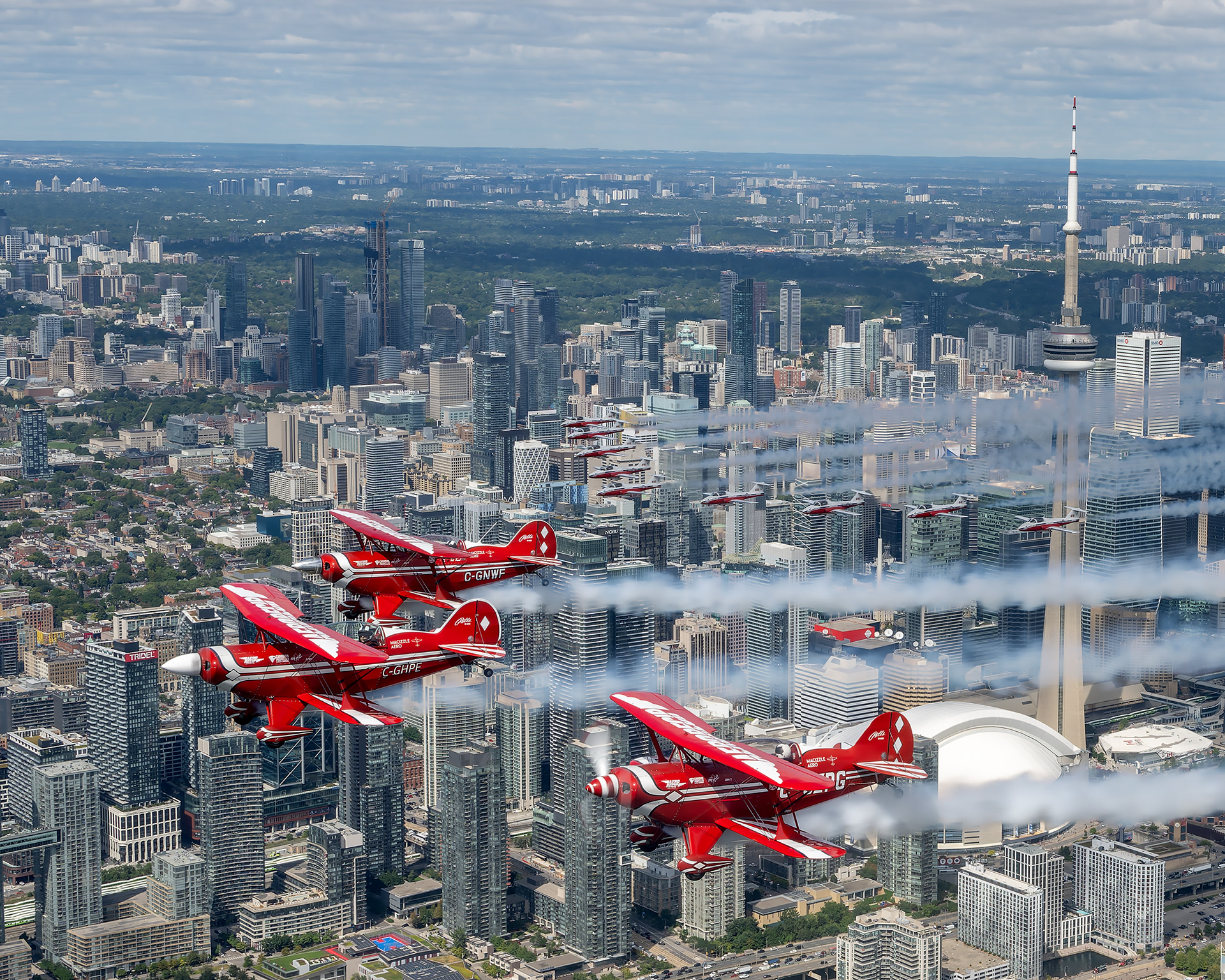 Air-to-air photography of the Northern Stars Aeroteam Pitts Special biplanes flying in close formation with the Canadian Forces Snowbirds over the Toronto skyline and CN Tower. Aviation photography by Kevin Prentice.