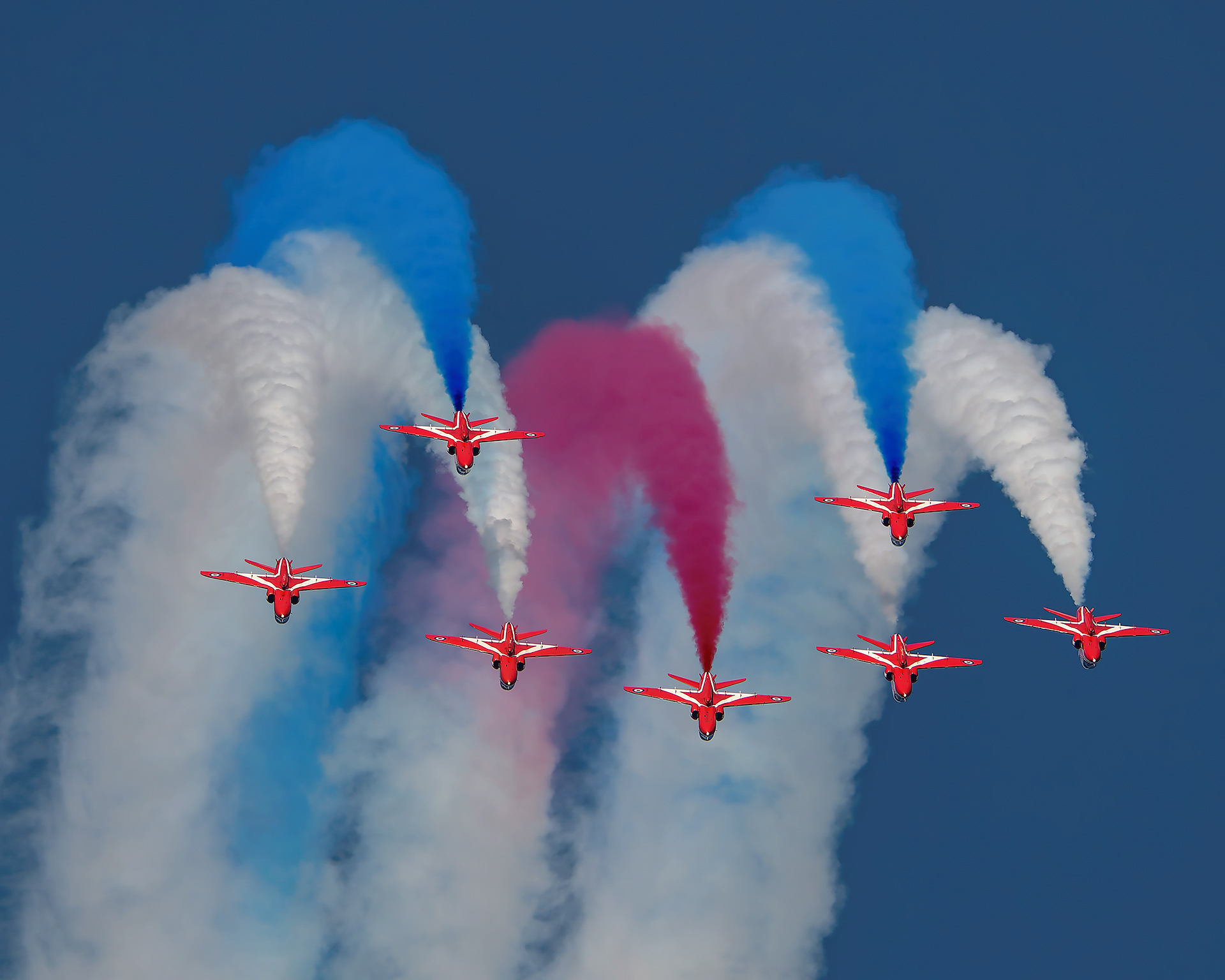The Royal Air Force Red Arrows aerobatic team performing a precision formation flight with smoke trails during an airshow display.