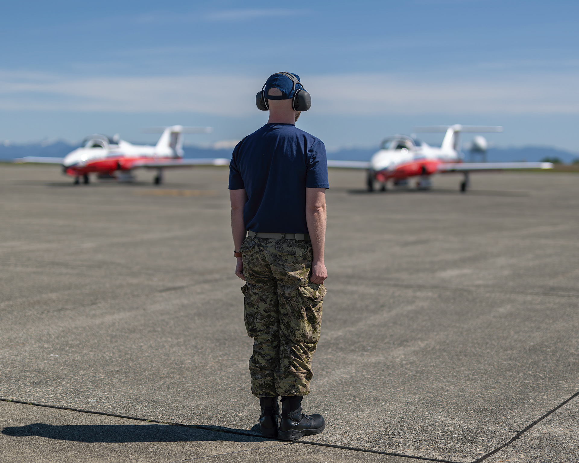 A Canadian Forces Snowbirds technician stands at attention on the tarmac as CT-114 Tutor jets prepare to taxi during spring training at CFB Comox, British Columbia. Fine art aviation photography by Kevin Prentice.