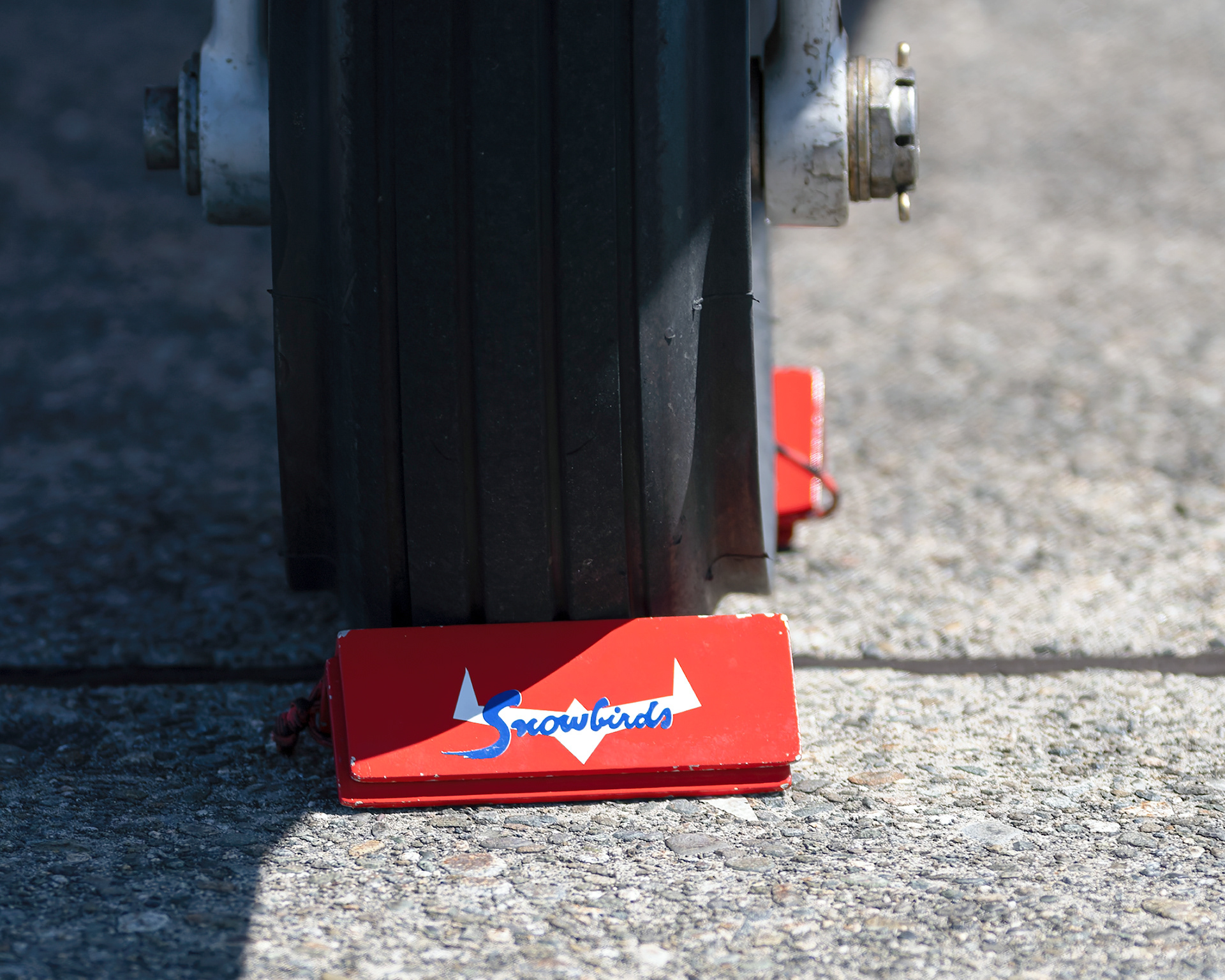A macro detail shot of a Canadian Forces Snowbirds CT-114 Tutor jet tire secured by a custom-branded red wheel chock on the flight line during spring training at CFB Comox. Fine art aviation abstract photography by Kevin Prentice.