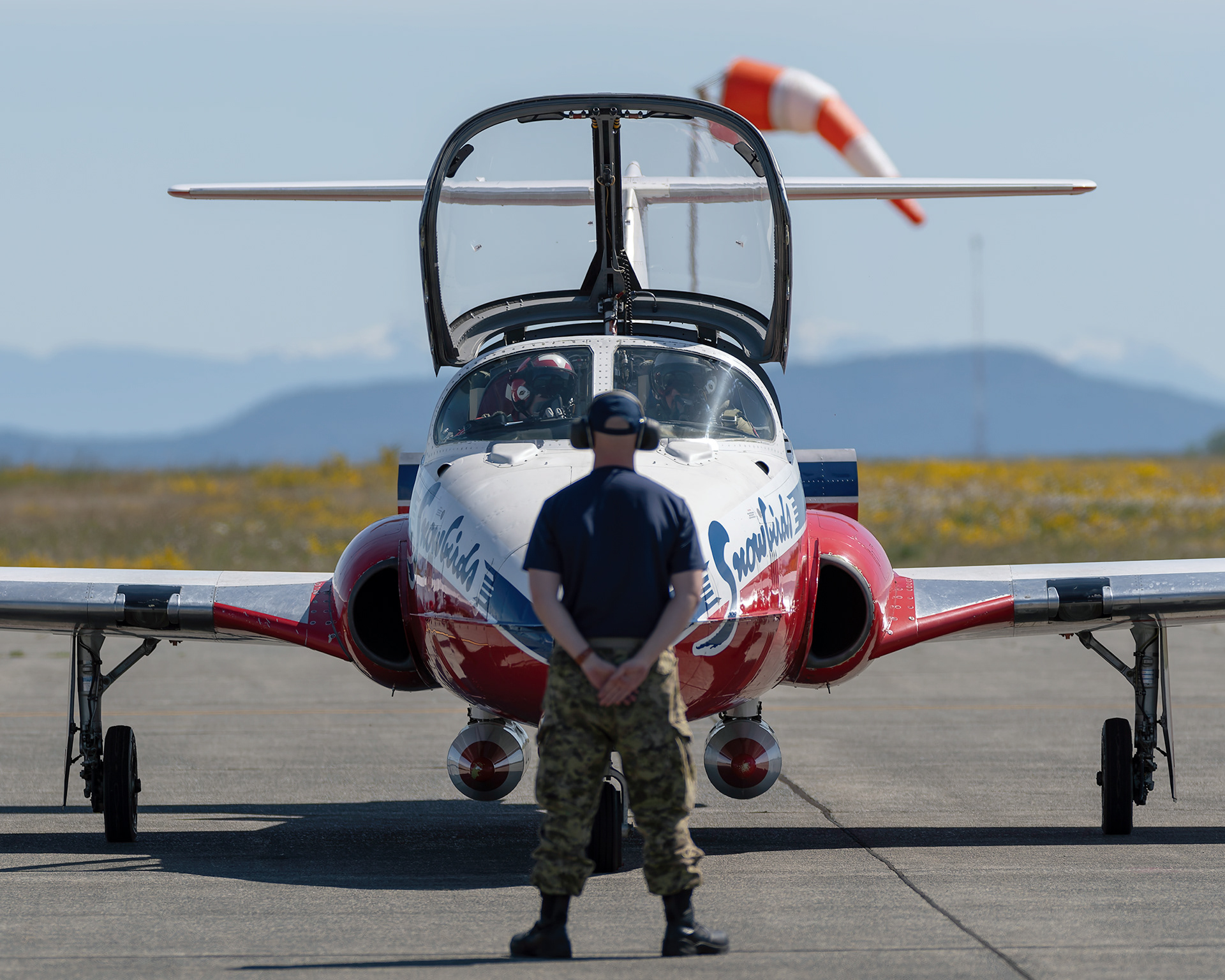 A Canadian Forces Snowbirds technician stands at attention on the flight line in front of a CT-114 Tutor jet during 2026 spring training at CFB Comox, British Columbia. Fine art military aviation photography by Kevin Prentice.
