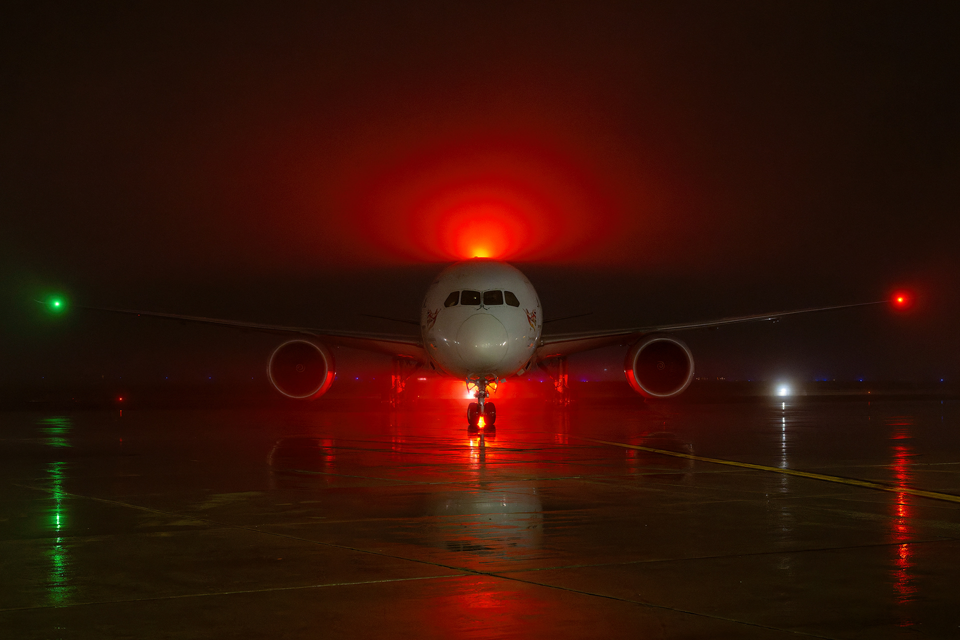 A Virgin Atlantic passenger airliner sits shrouded in dense night fog on the wet tarmac at Toronto Pearson International Airport (YYZ), illuminated by the powerful crimson glow of its anti-collision beacon light. Commercial aviation photography by Kevin Prentice.