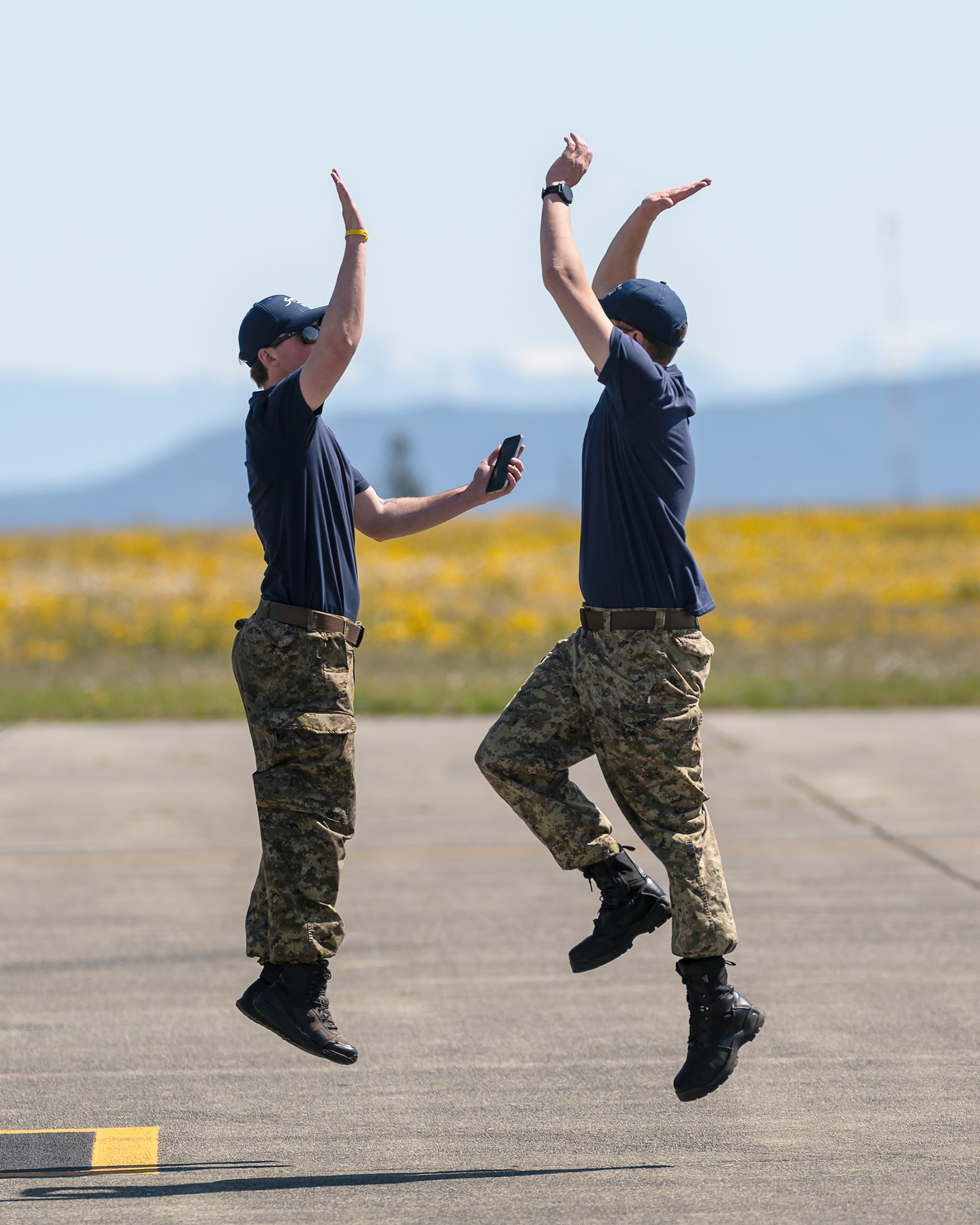Two Canadian Forces Snowbirds technicians jump to celebrate a successful launch of the team during 2026 spring training at CFB Comox, British Columbia. Fine art aviation lifestyle photography by Kevin Prentice.