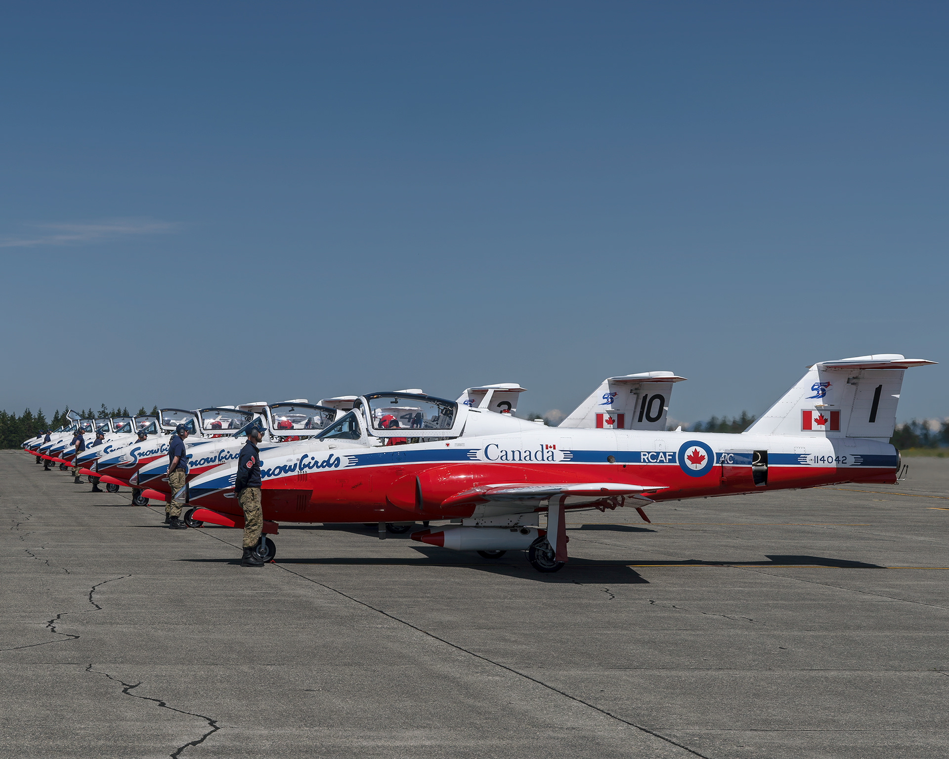 A pristine line of Canadian Forces Snowbirds CT-114 Tutor jets sits on the flight line as technicians conduct final pre-flight checks before a practice launch during 2026 spring training at CFB Comox, British Columbia. Fine art aviation photography by Kevin Prentice.
