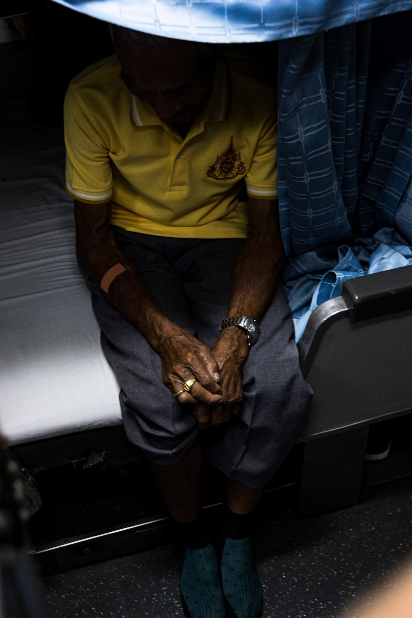 An old man sits opposite his son (who is below me) on the lower bunk of a train departing from the station in Bangkok. He reminded me of an aged, beloved pet—a dog or cat—that because it is so weak, frail, and thin needs care and guidance for nearly everywhere it goes.