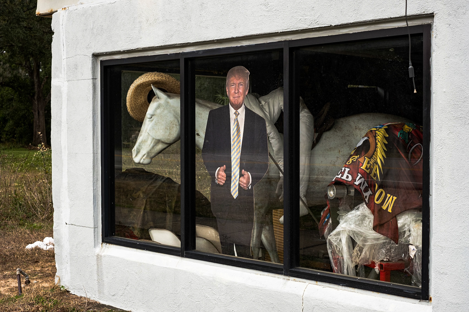 Bicycling America XI. Cardboard Cutout of Donald Trump amidst an Assortment of Stuff in a Shop Window on the Outskirts of Pensacola, FL, December 2018. I took this photograph leaving Pensacola after spending a blissful and relaxing two or three days there at the First United Methodist Church I do believe. The man running the youth program there had done several bicycle tours in the past, and had a WarmShowers profile offering space in one of their buildings for travelers to stay, though, either he is no longer there, or they are no longer allowing that, since I'm not seeing the profile on WarmShowers right now. Regarding the photograph, I just thought this was an amusing, nonsensical collection of compositional elements, and being as our current president IS basically a cardboard cutout in mind, body (well, maybe not body) and soul, this just feels timely and right to post. Also, surrealistic picture, surrealistic presidency.