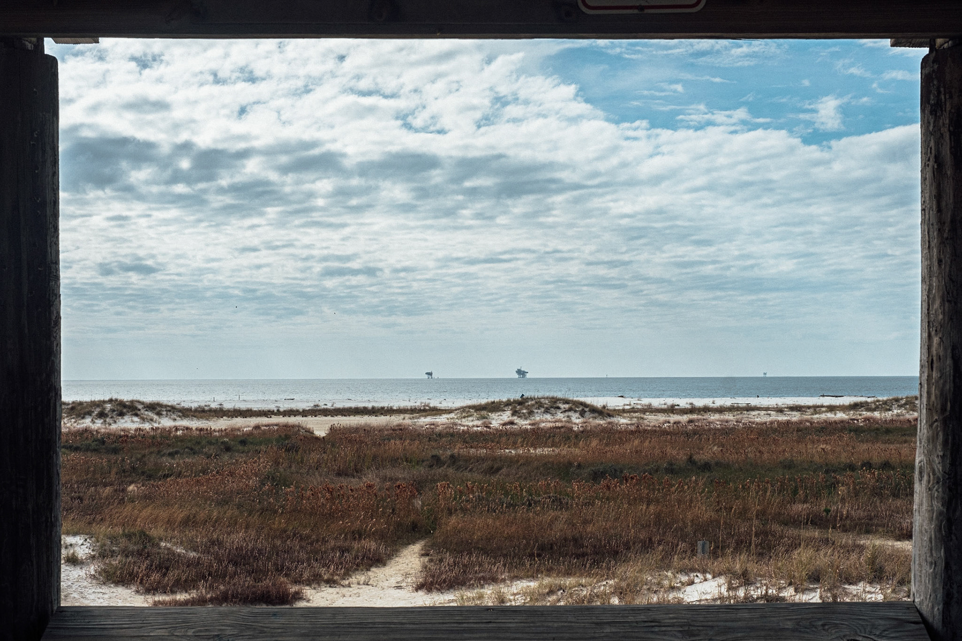 (Mostly) Bicycling America XXXII. Oil Rigs in Gulf of Mexico, Dauphin Island, Alabama, December, 2018. Well, as per my last post, this was shot while I was on Dauphin Island. There was a beach near where I was staying (well, there was beach everywhere, as the island was quite narrow) with a bunch of these large, covered gazebos that were up on stilts, which gave one a heightened view of the surrounding beach and waters. I used the railing, roof posts, and bottom edge of the roof as framing guides for this shot. Turned out quite nicely I think! Words can not explain at my shock at the number of oil platforms out there (not just in this picture); they're EVERYWHERE, and at night light up the horizon like the lights of small villages seen from a mountain pass in the distance.