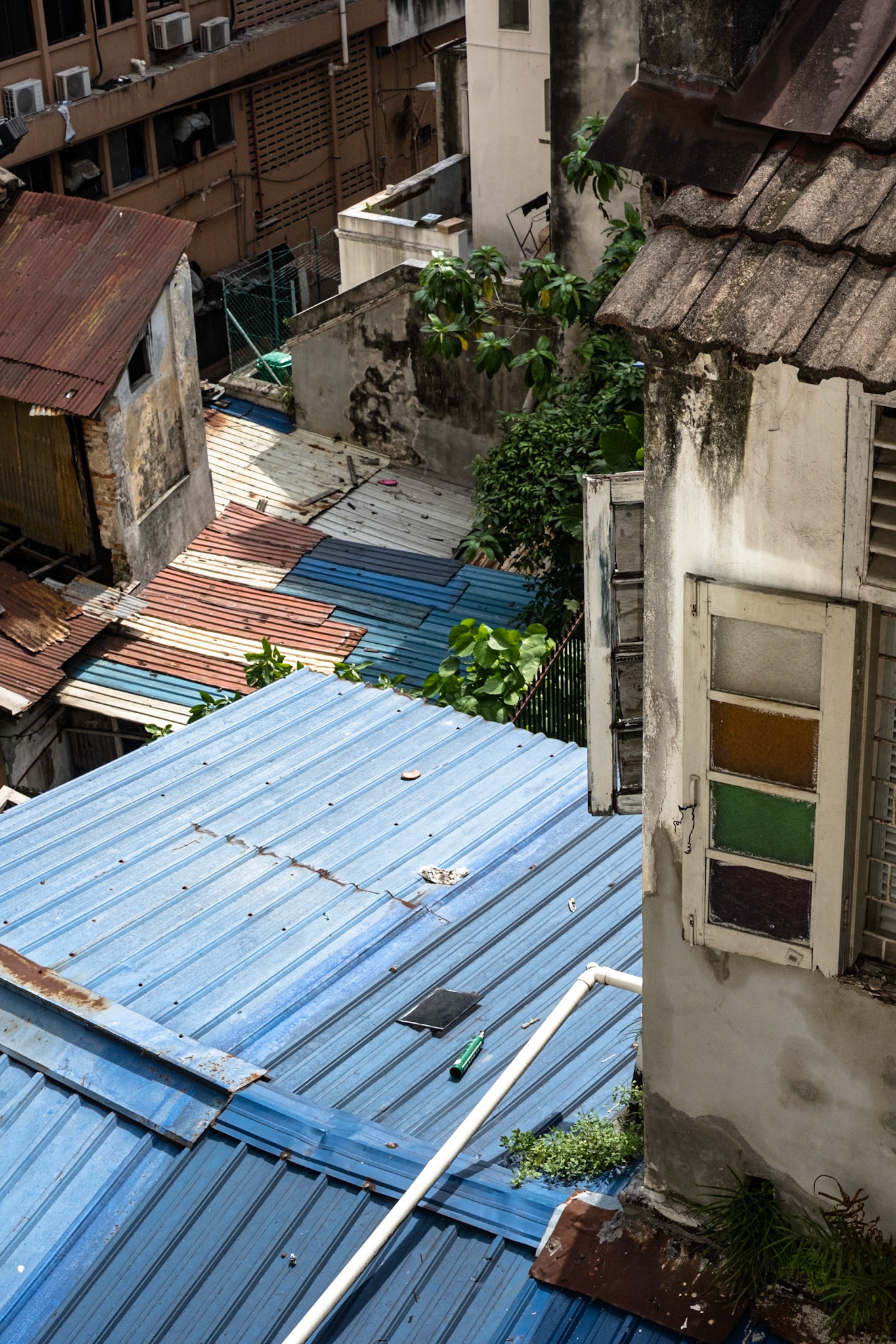Revisiting Kuala Lumpur VIII. View from the window of the room in the hostel that I work exchanged at. I really liked the four panes of colored glass (well, three panes of colored glass), and the tile roof of the buillding on the right side of the frame. And the colored aluminum/steel/plastic(?) panels used as roofing, and the plants. This view just fascinated me my whole stay. Of course it's only part of the view.