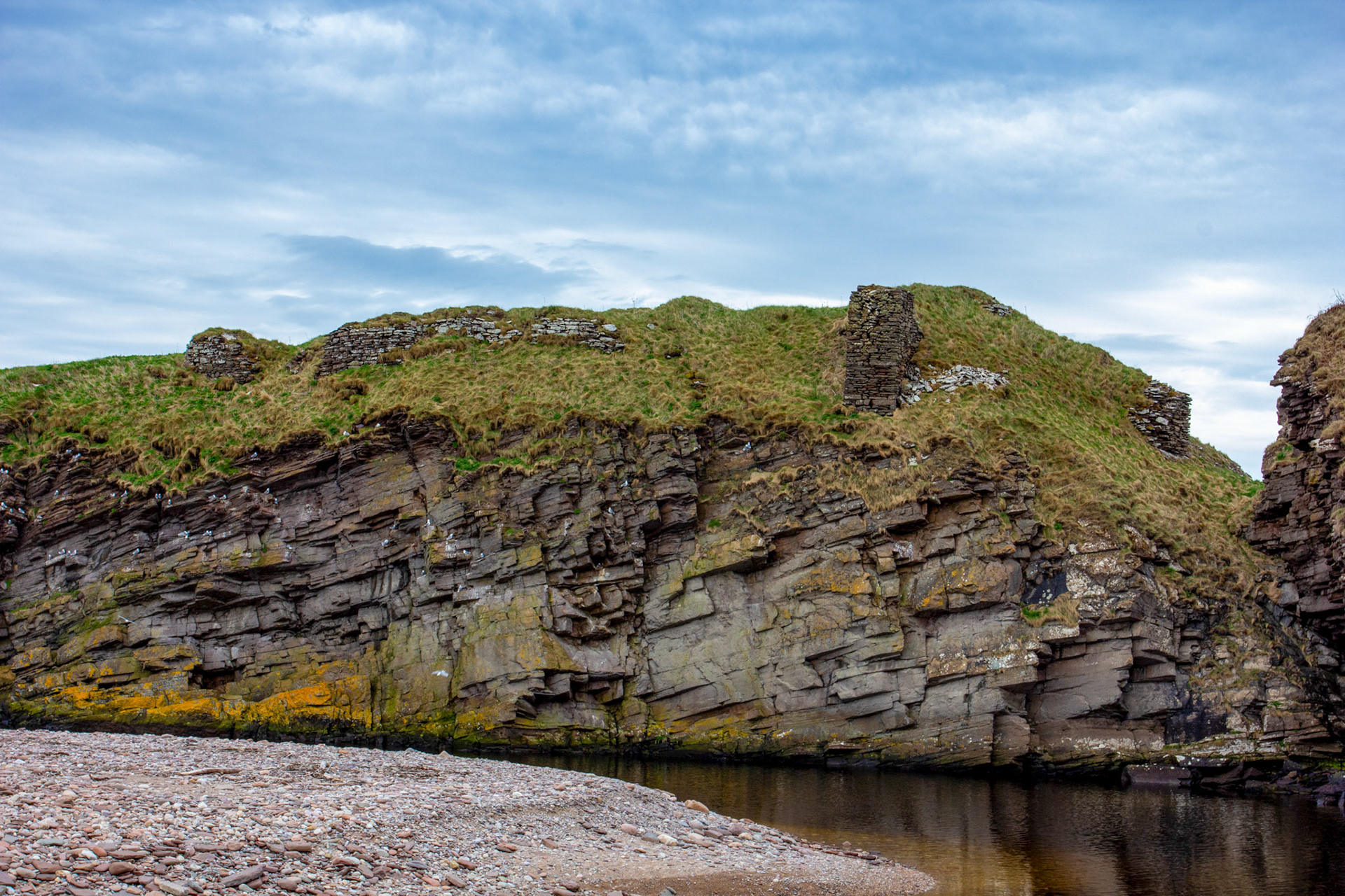 Berriedale Harbour 01 May 2026On a tongue of rock projecting across the mouth of the Berriedale River are the remains of Berriedale Castle. The promontory on which the castle stood has been cut off from the high ground in rear of it by a deep ditch across the neck. There has been a double row of buildings along the promontory separated by a narrow courtyard, and the whole enclosed by a wall of enceinte, still partly traceable. The remains are very scanty.Berriedale Castle belonged in the 14th century to Rannald or Reginald Cheyne, thereafter passing through marriage to the Sutherlands and subsequently to the Oliphants. In 1526 Andrew Oliphant sold the property to his uncle, Laurence, Lord Oliphant, and in 1606 his successor sold Berriedale etc to the Earl of Caithness.D MacGibbon and T Ross 1887-92; W Macfarlane 1906-8; RCAHMS 1911.Berriedale Castle: Fragments of a massive enceinte wall (2.5m thick) can be traced here and there all round the promontory, but mostly on the W side. A turf-covered retangular foundation, 14 by 4.2m, lies on the E side abutting the cliff. On the W side, the footings of a range of buildings, 0.8m high, exist, at least three compartments being noted amid the rubble and grass. A small gatehouse, some 3.4m square, existed at the S end, but only the footings, 0.2m high, remain. On the N side of the rock-cut ditch are the remains of an abutment of a bridge which crossed the 6m wide gully. About 20m E of the gatehouse, and at a lower level, are the remains of a building with an apsidal-ended W end, 1m high. It was about 12m long by 3.5m broad, only a fragment of the N wall remaining, 3.5m long by 1m thick and 0.5m high. The E end terminates abruptly in a rock face.