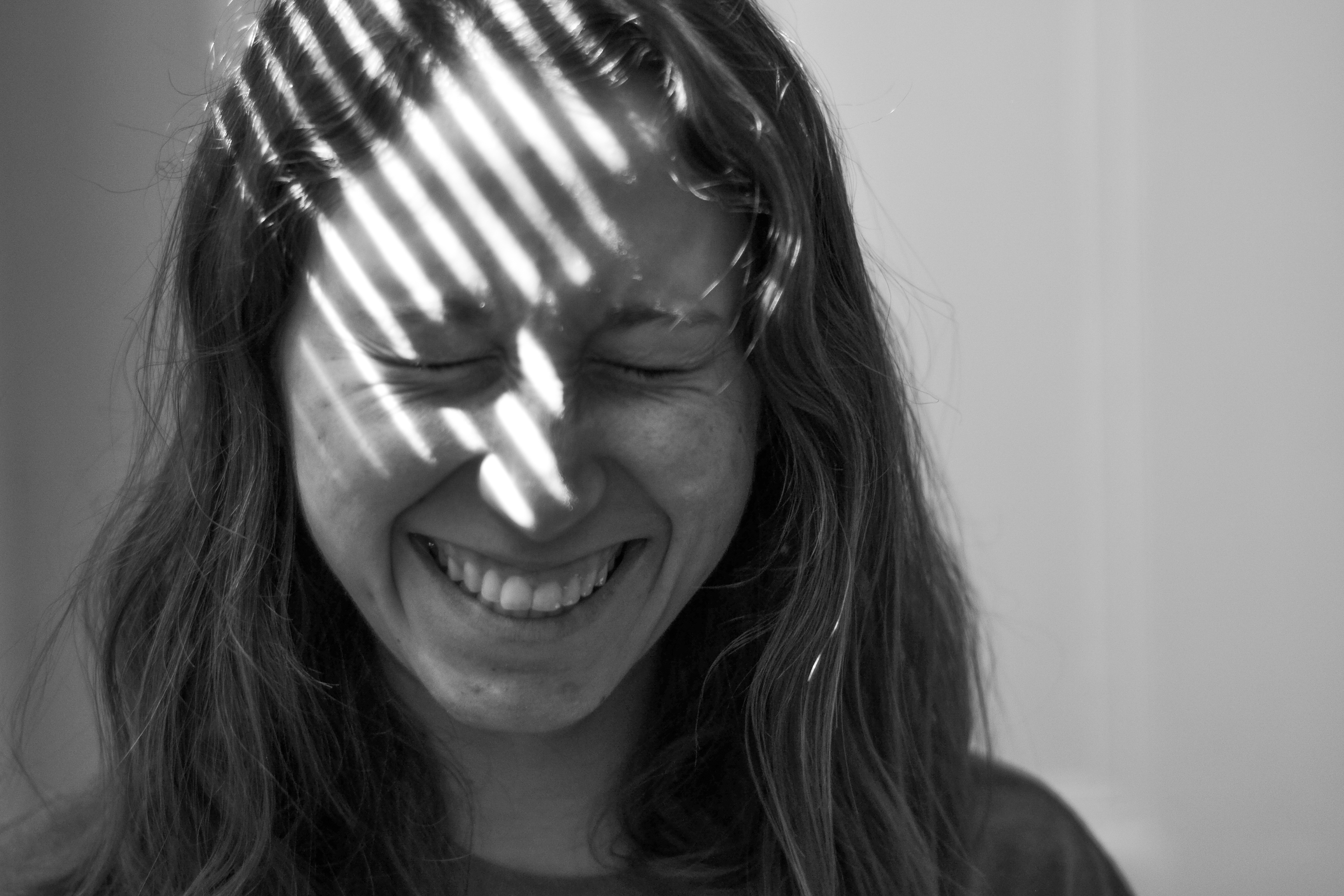 Natalie Reeder, 21, poses in the shadow of the blinds in her Mission Hill home on April 7, 2020. Reeder, who does not generally like posing for photos, shares a candid laugh with the camera at the end of the shoot.
