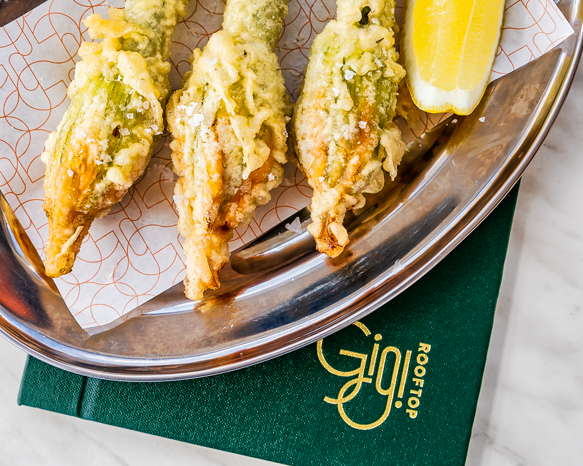 Zucchini flowers on a metal plate with a lemon wedge.