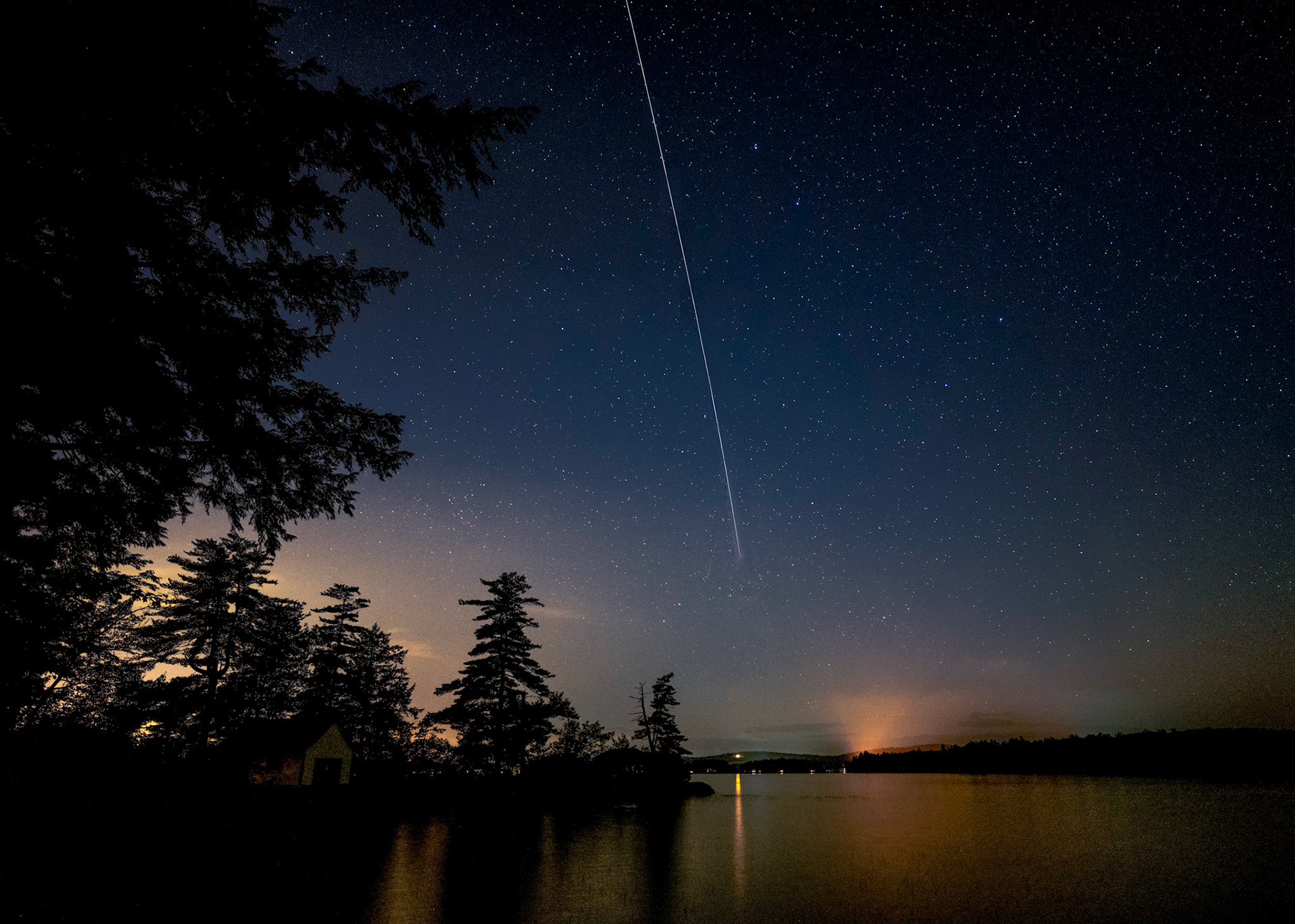 A satellite is captured as it moves across the night sky off of Sunset Point on Lake Wentworth