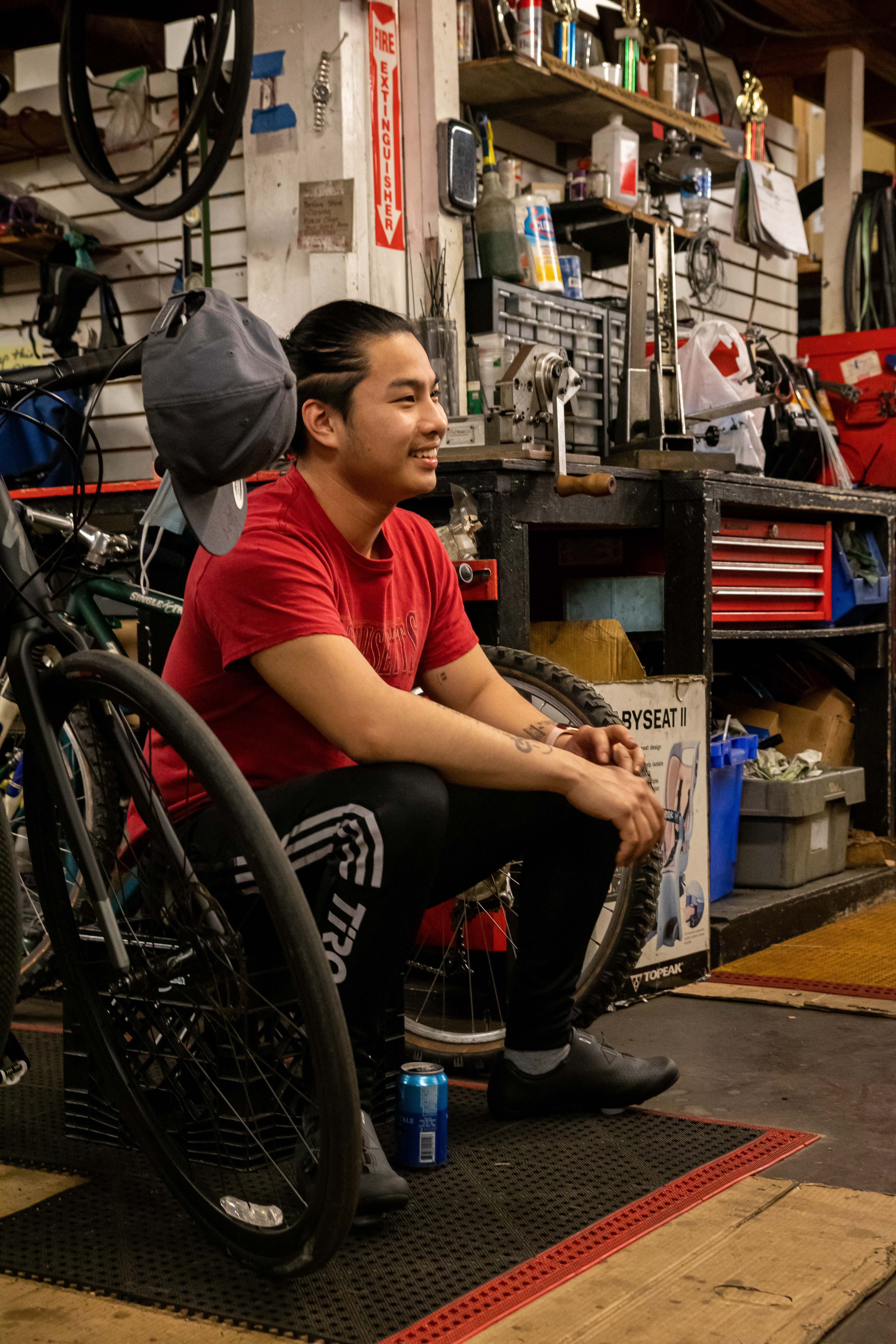 Andy Qiu smiles at a remark made by another mechanic after the shop is closed for the day, April 15, 2022 at Community Bike Supply, Boston, Massachusetts. The mechanics gather in the warehouse for a quick destressing period with some beers before heading home for the night.
