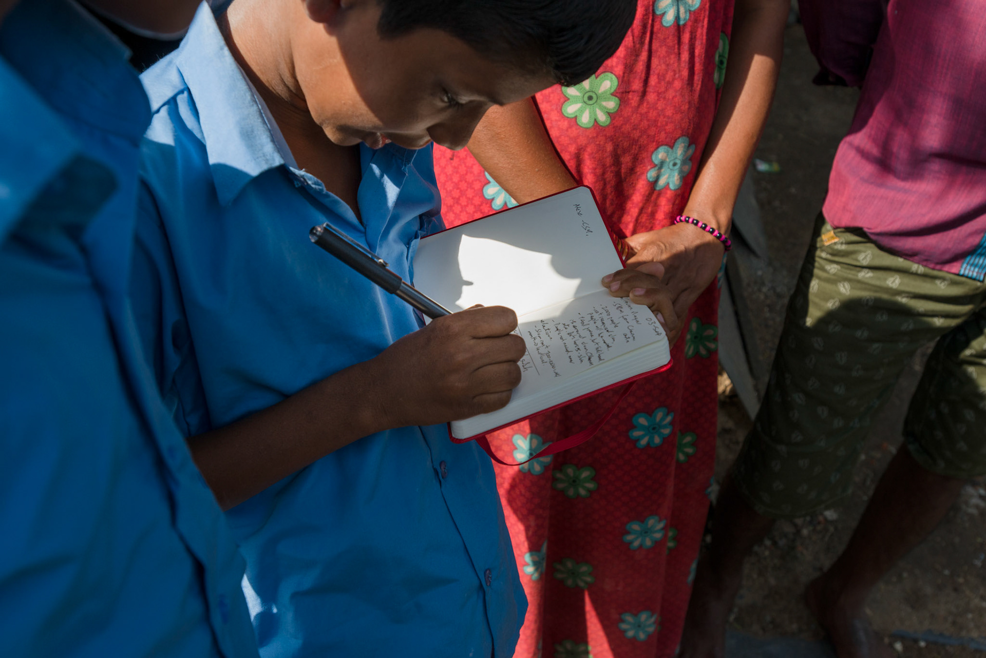 Vasanth, ready for school, writes his parents' and brother's name in my notebook. His parents handed him the notebook when asked for the names.