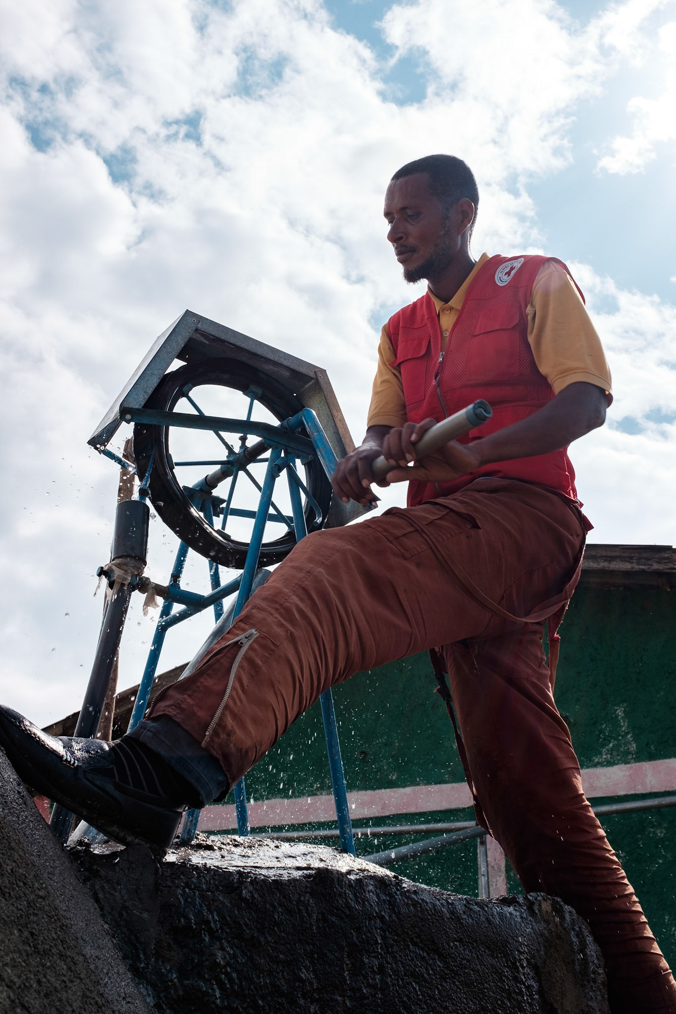 A man pumps water from the tank to the filling pipe while women and children fill their water cans.
The water tank collects rain water from the roof of the adjacent building. This water point saves the local people much time in collecting water.
