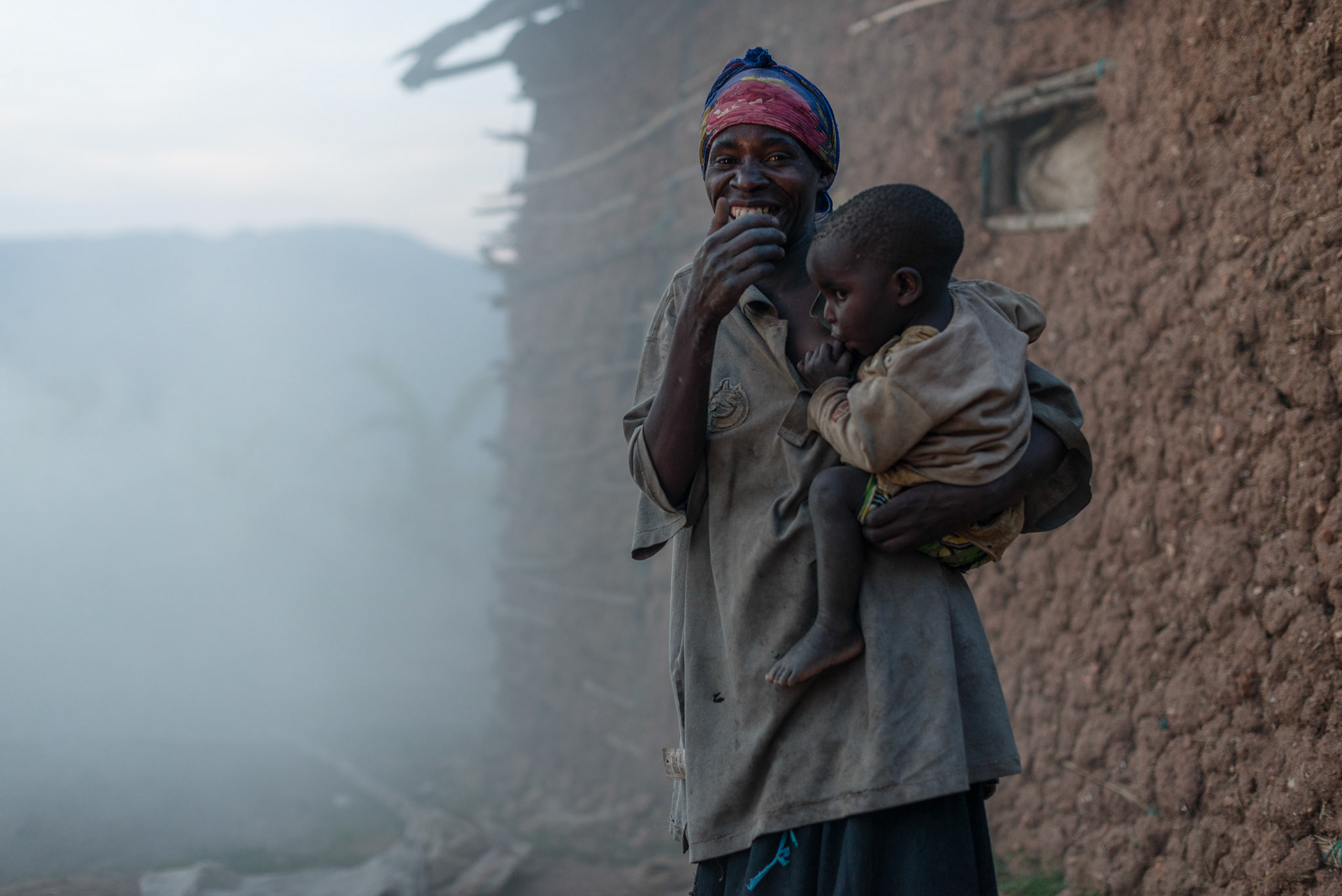 Philomene stands in the smoke from the green grass placed on top of the pots during firing.