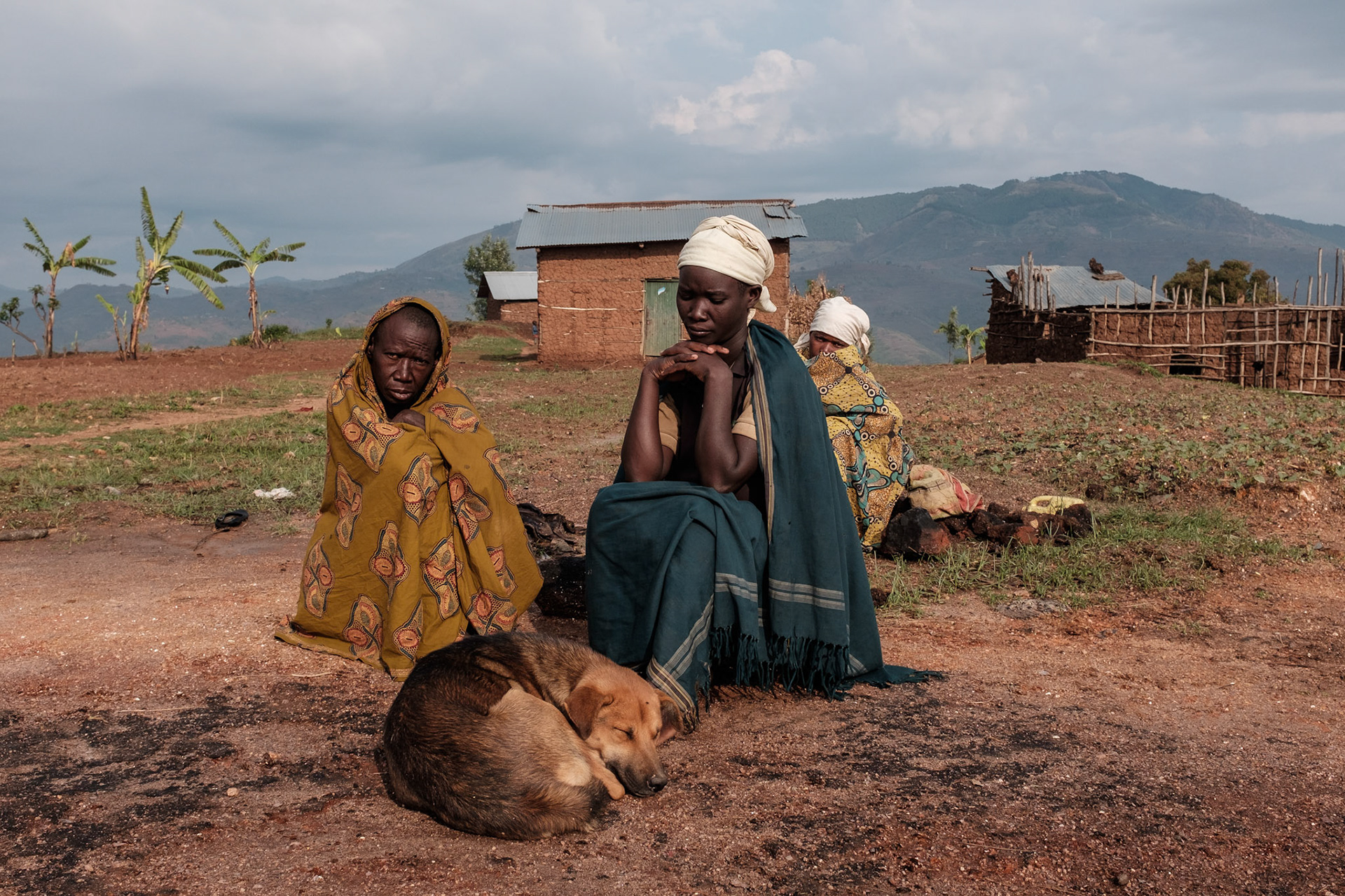 Kasebuturanyi is one of the poorer villages in the region. The soil is not as fertile as other areas, and being harder requires more manual labour to work.
Here, Laurencia, 53, Ancille, 31, and Chantal, 29, warm themselves in the morning sun with Simba.