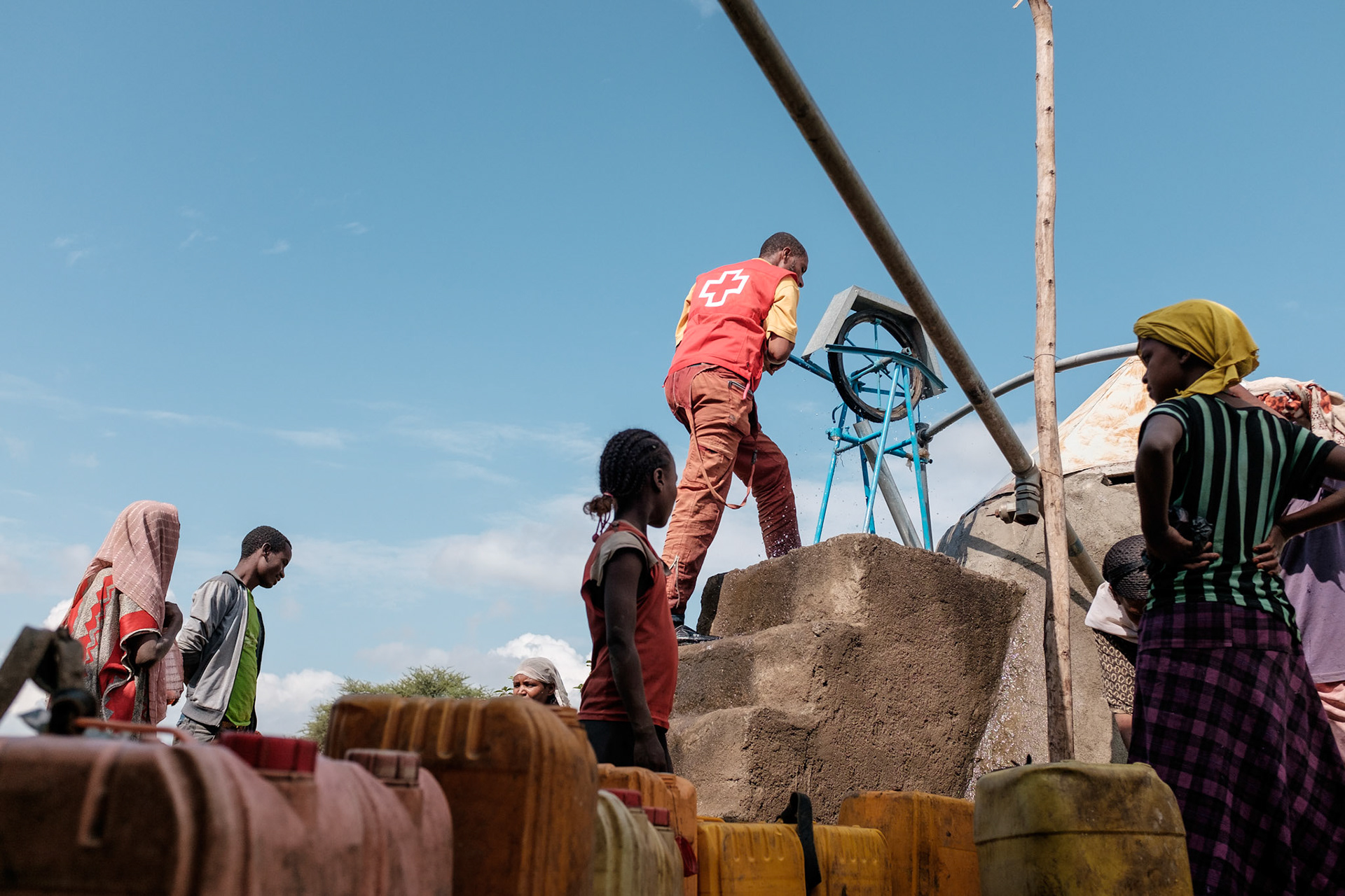 A man pumps water from the tank to the filling pipe while women and children fill their water cans.
The water tank collects rain water from the roof of the adjacent building. This water point saves the local people much time in collecting water.