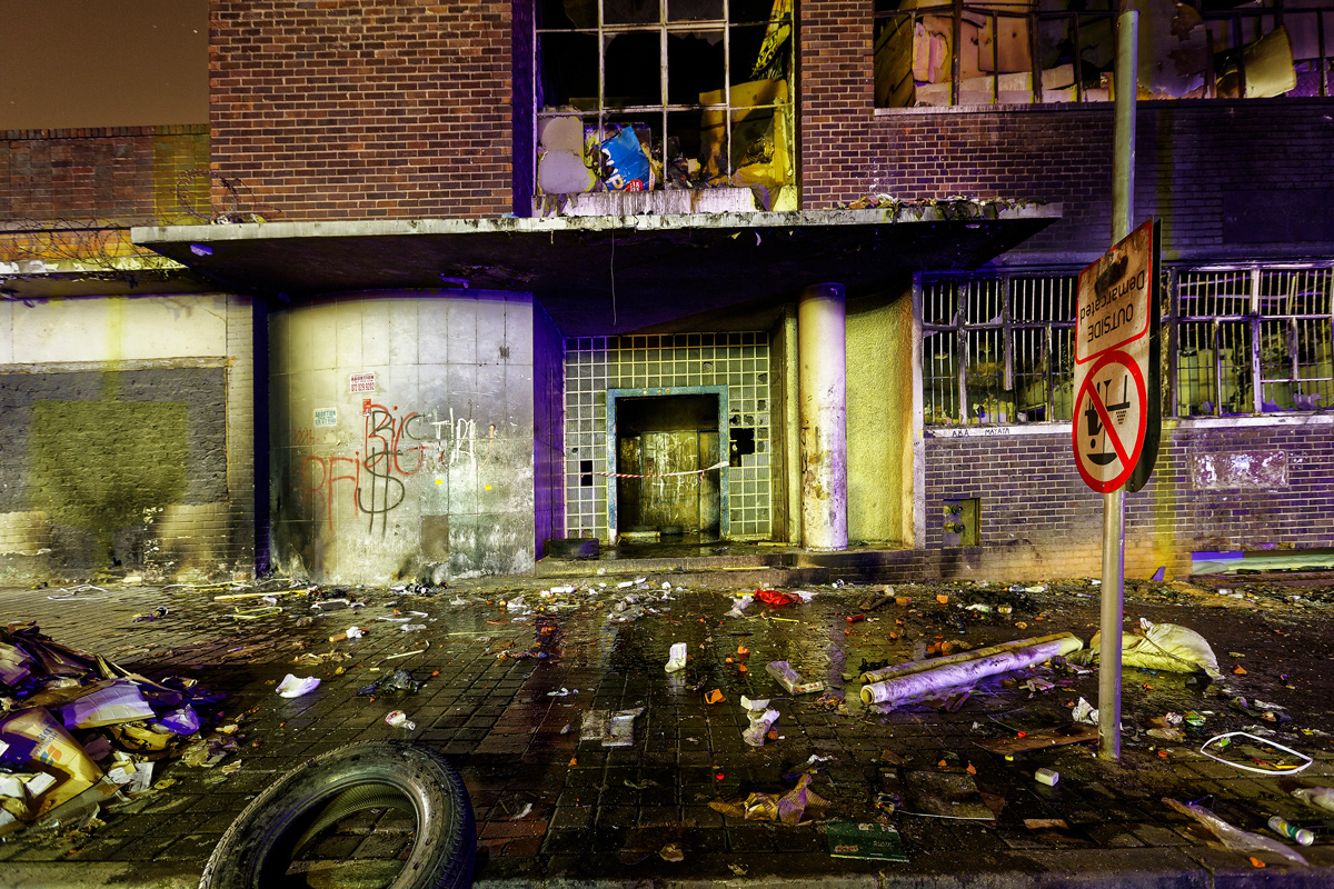 Enter Dark City 2014- 2016 Photographic Print Fine Art Cotton Rag A1. The entrance of Dark City photographed on the night an angry mob of residents from the surrounding flats attempted to burn down the building with petrol bombs. The entrance of Dark City was enough to stop persuers following a mugger back into the building and was very much a barrier to those unaccustomed to Dark City. It was also used for ambush and a victim would be pulled into the building to be mugged of everything including their shoes.  