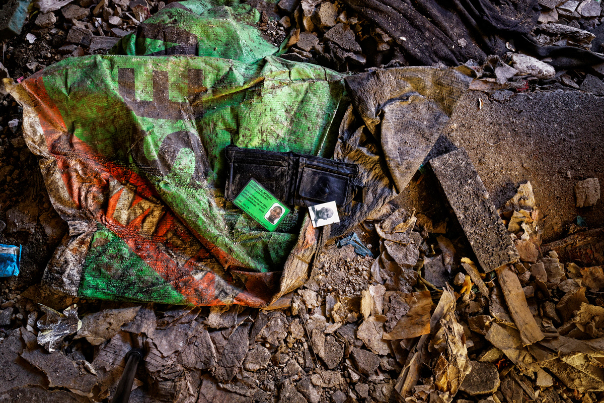 Norman The Forlkift Driver 2014 - 2016  Photographic Print UV Print, Lightbox 850mm x  850mm. The victim of a mugging's wallet lies on the ground floor of Dark City. His permit card to operate a forklift lies next to his ID photograph. The wallet has clearly been sorted through and abandoned in an eerily reflective manner of its former owner. This image speaks about crime in Dark City. 