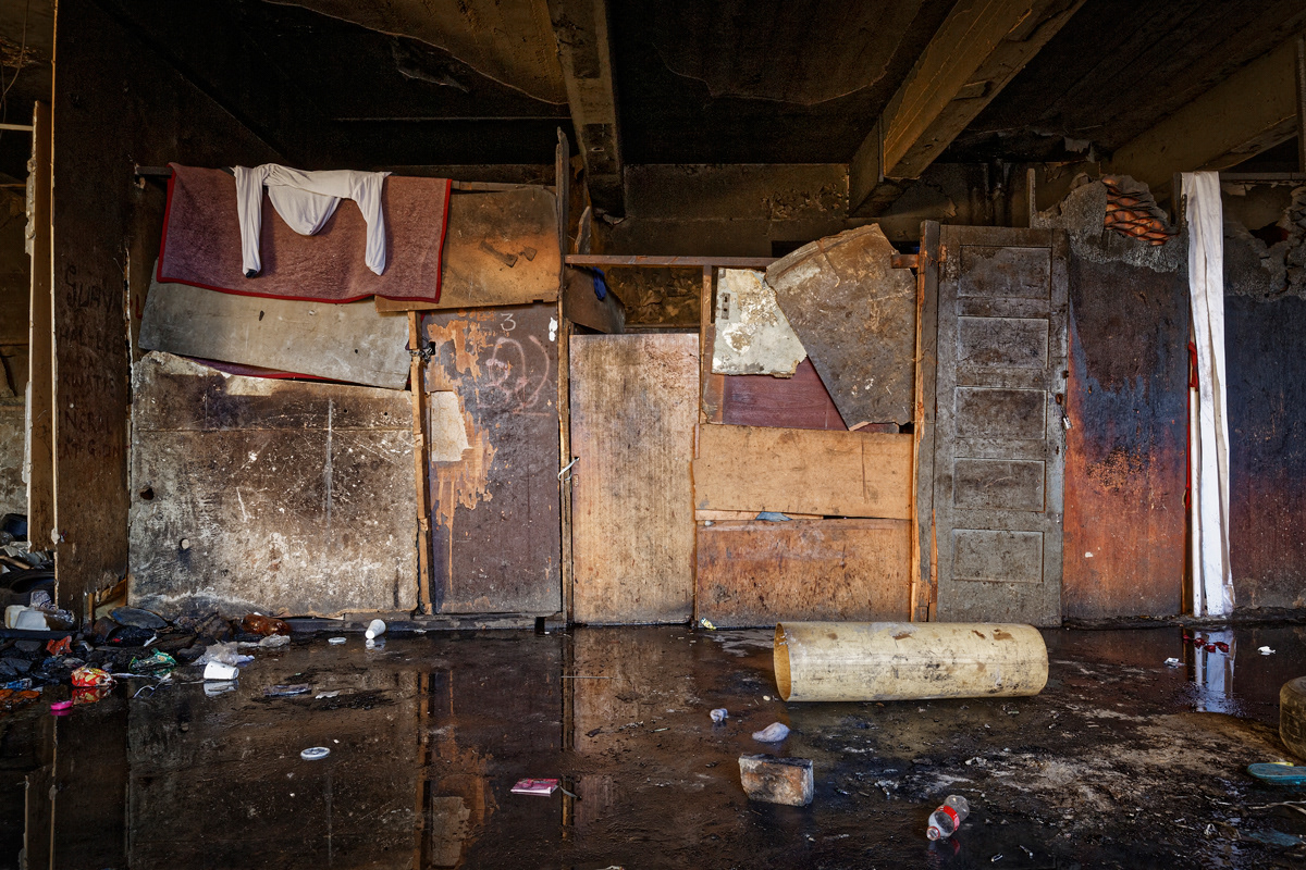 Ground Floor Shacks 2014 - 2016  Photographic Print Fine Art Cotton Rag A1. Three shacks share supporting walls on the ground floor of Dark City. A damaged water pipe has flooded the basement, which was completely inaccessible and filled with trash. The water had begun flooding the ground floor and homes built there.