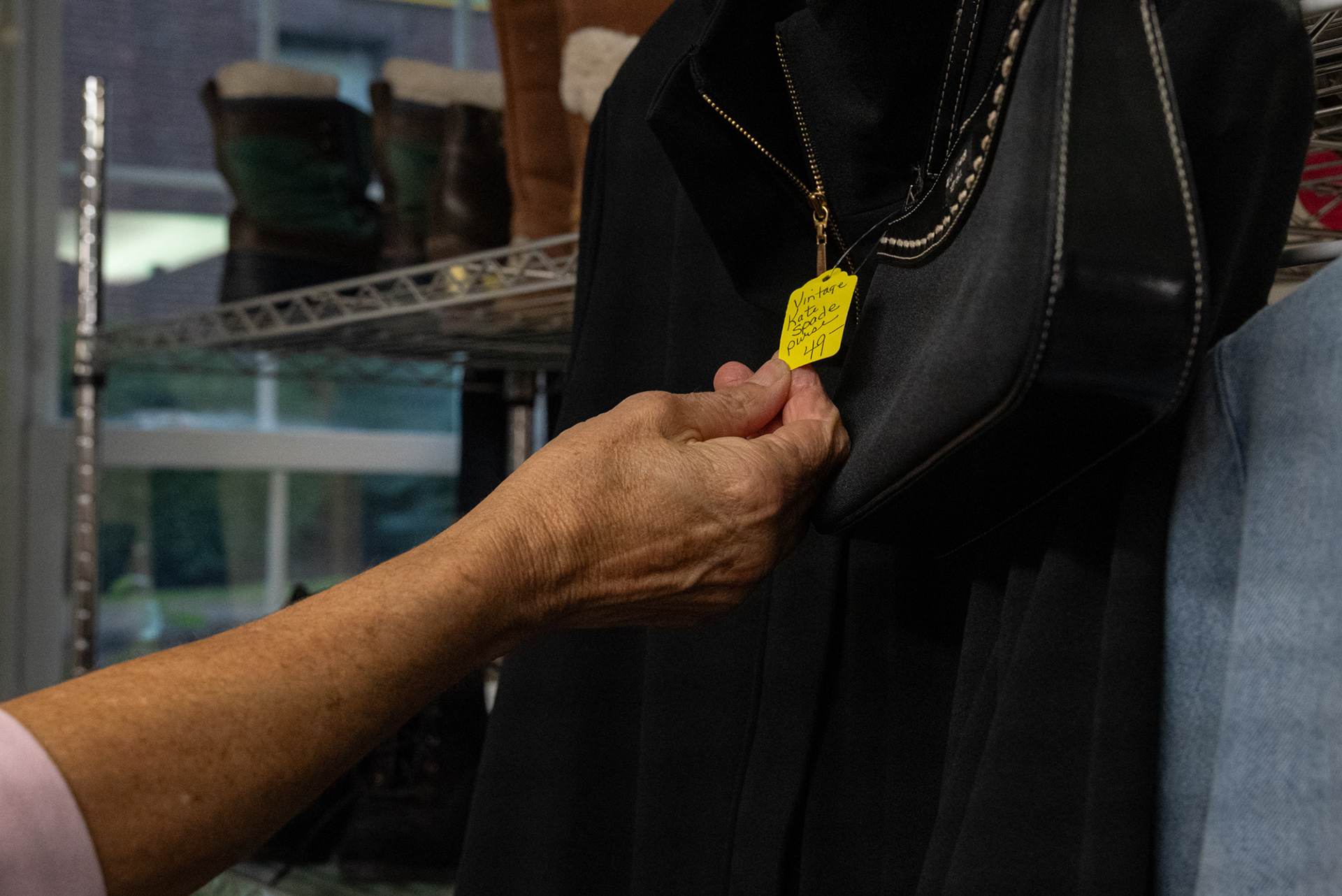 Volunteer Carolyn Legg holds a price tag on a purse. Each month items are discounted, after 4 months if an item is not sold, it is donated to charity.  The shop often donates to Dr. Weeks Elementary school and the Samaritan Center.