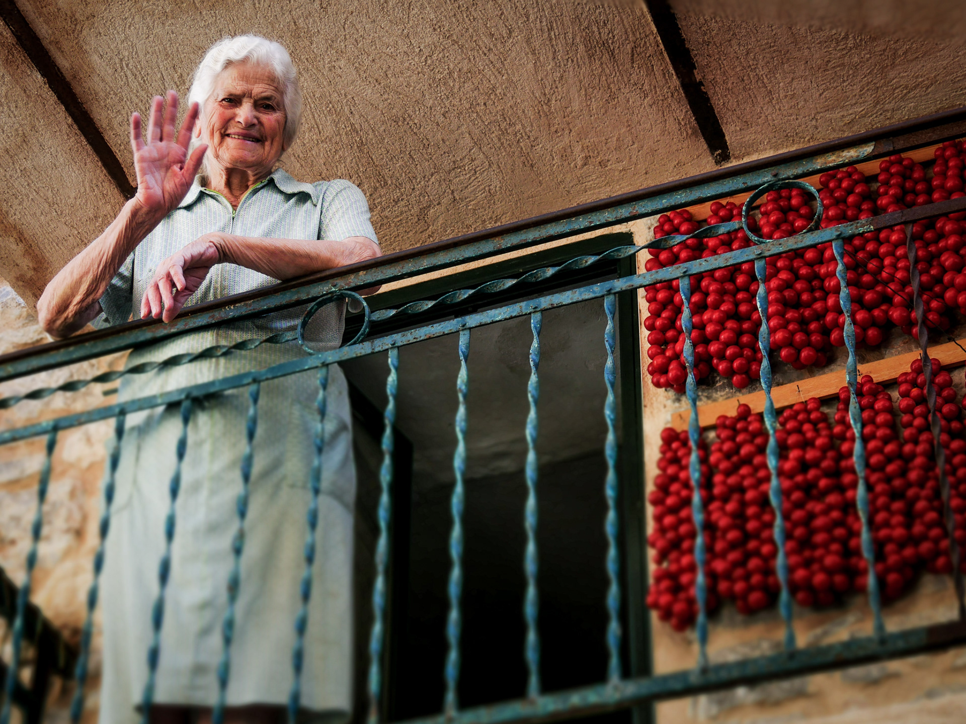Woman waving next to tomatoes drying on her balcony in the village of Pyrgi in Chios.