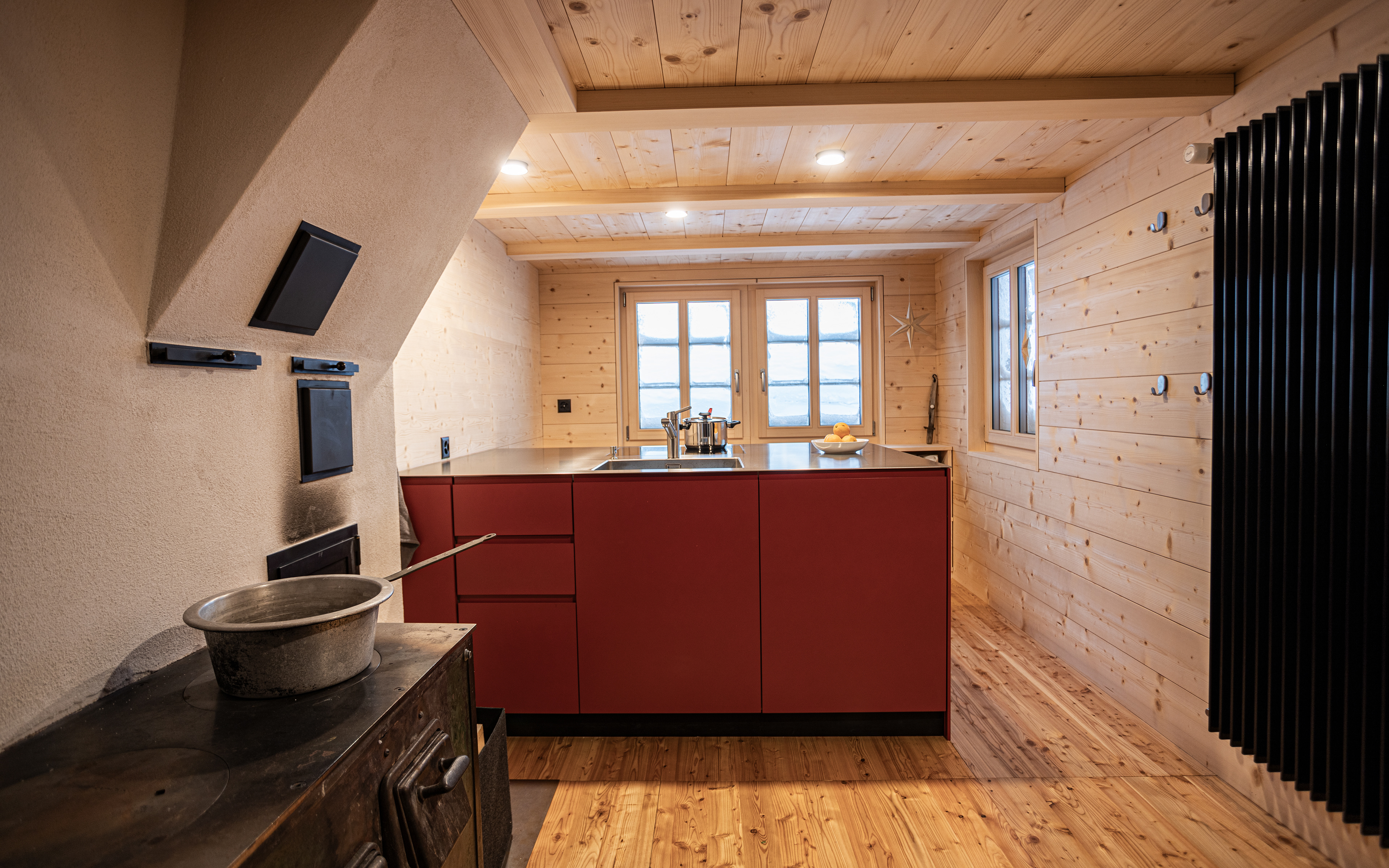 MKPHOTO, Architekturfotograf aus Aarau, Umgebautes Wohnhaus in Gadmen, Rote Kücheninsel neben restauriertem Holzherd. 