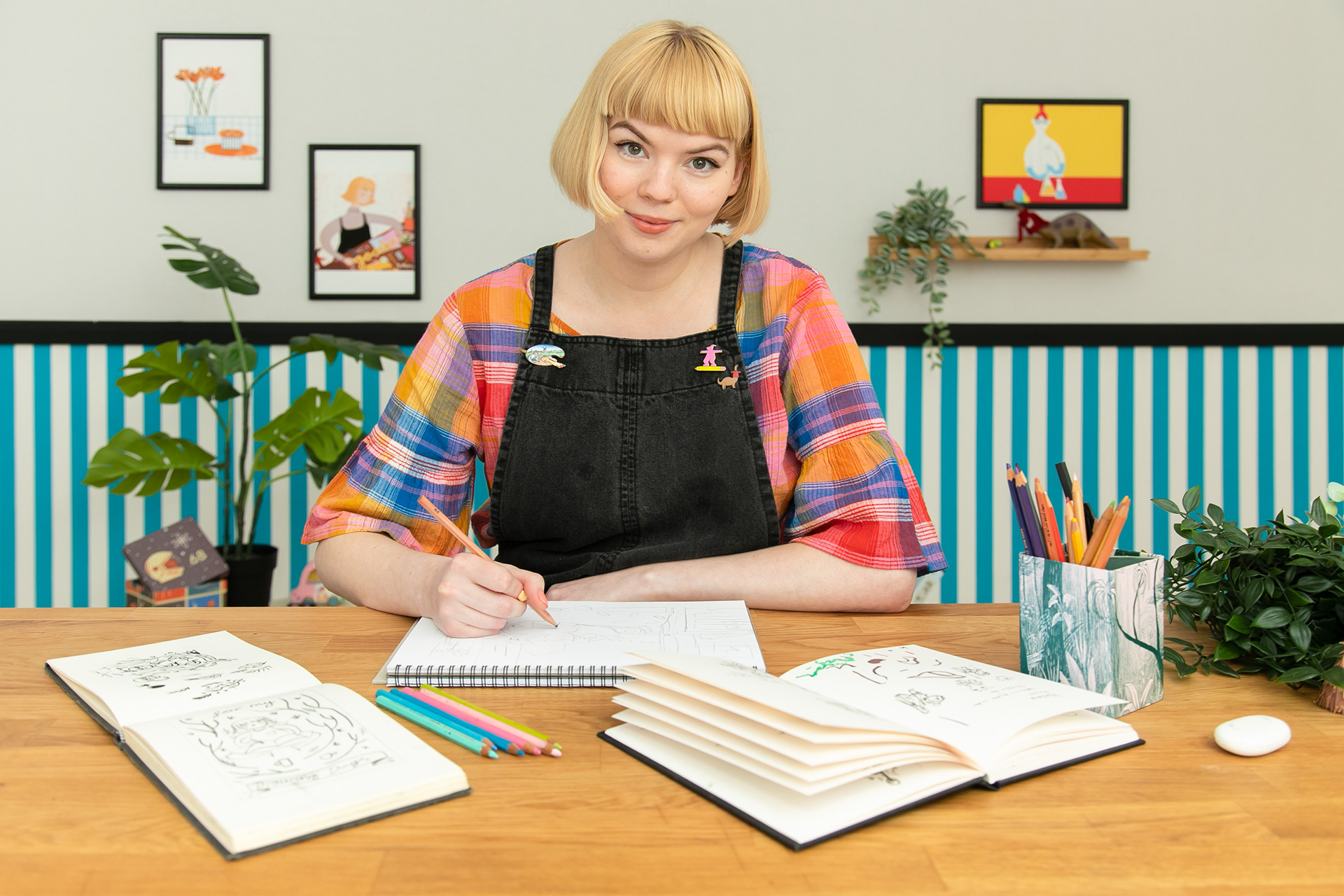 an image of me, a woman with short blonde hair and a fringe sat drawing at a desk.
