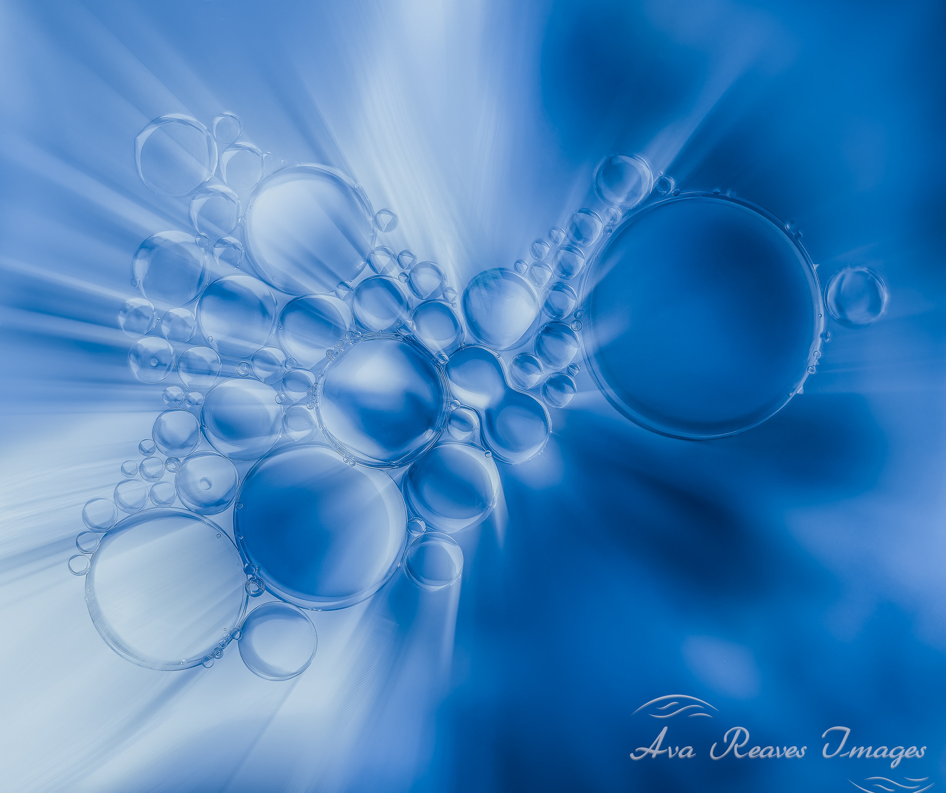 Macro photo of oil and water bubbles clustered on a light blue background with abstract light rays