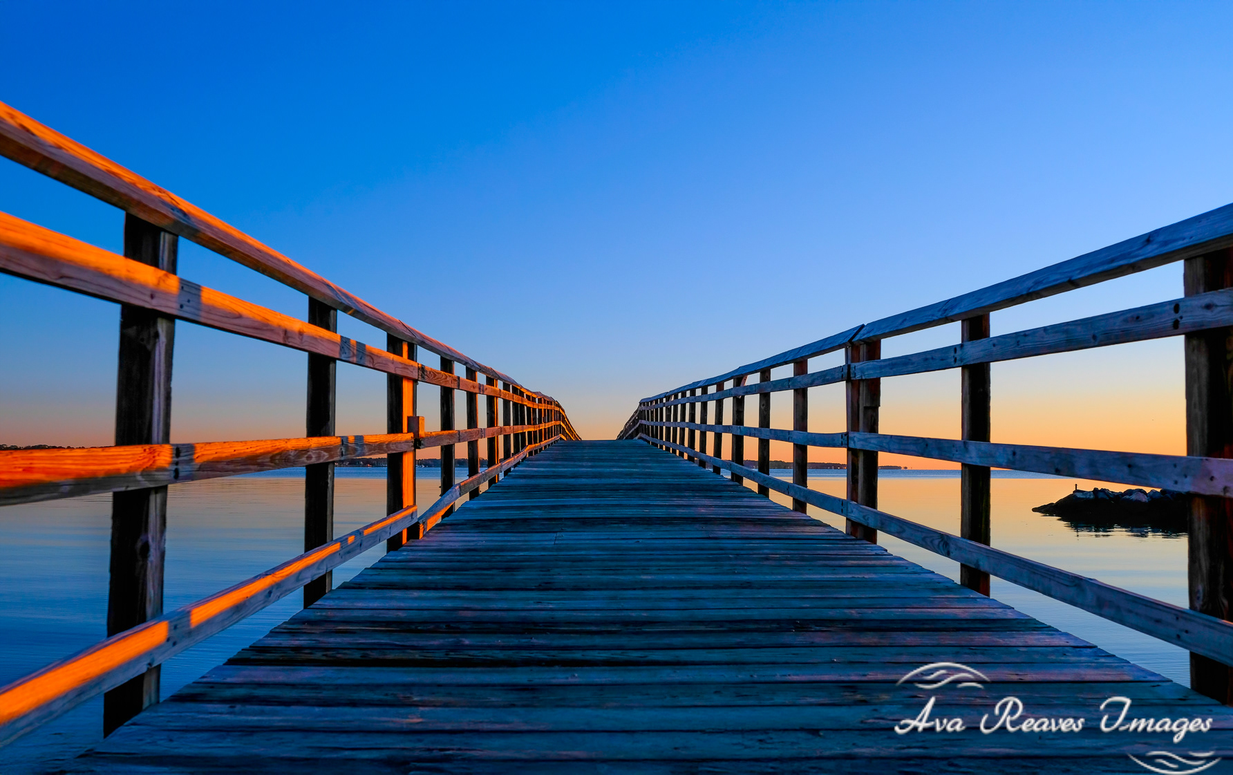 Wooden bridge at Yorktown Beach during sunrise with golden light on railings and calm water